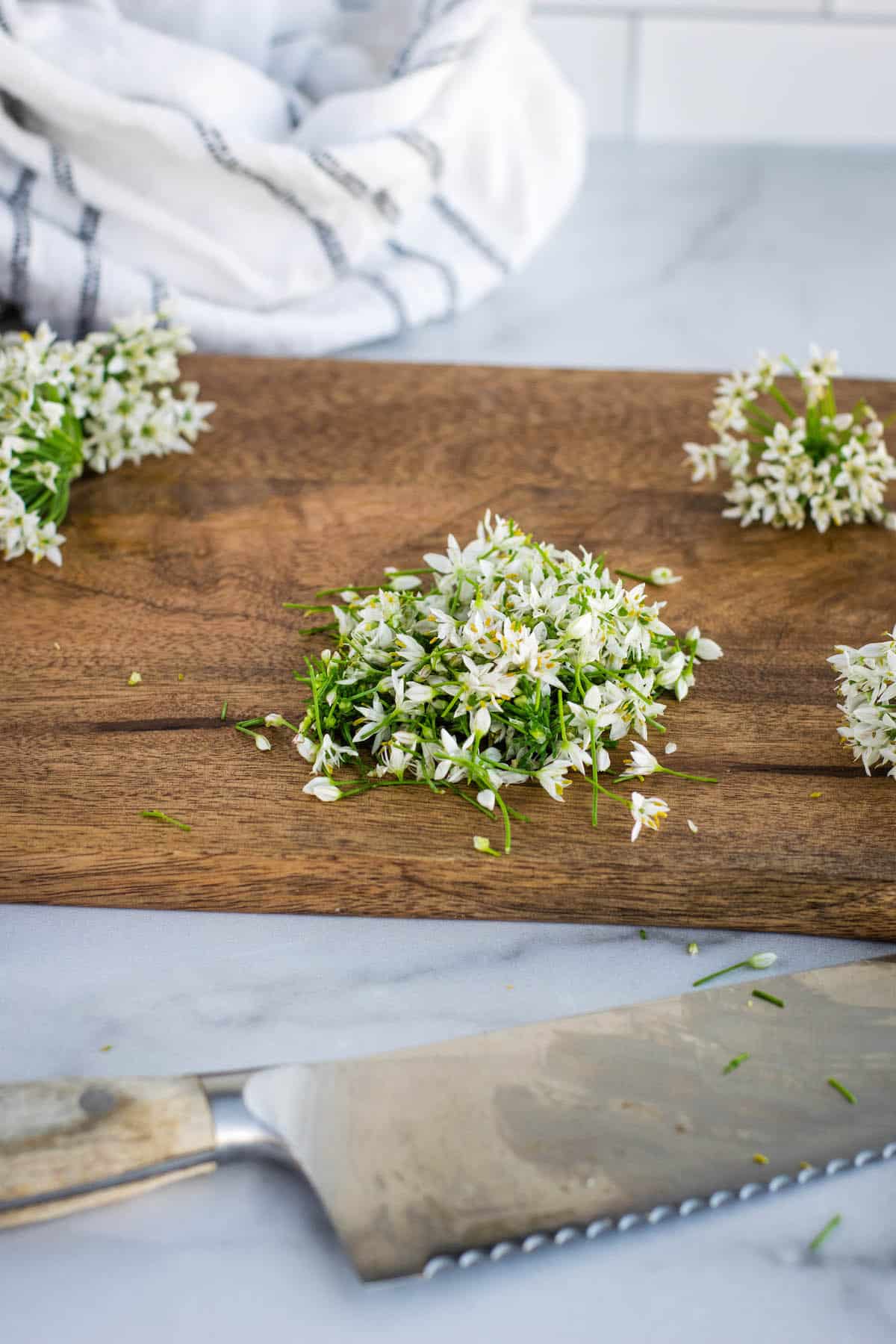 chopped garlic chive blossoms on a wooden cutting board.