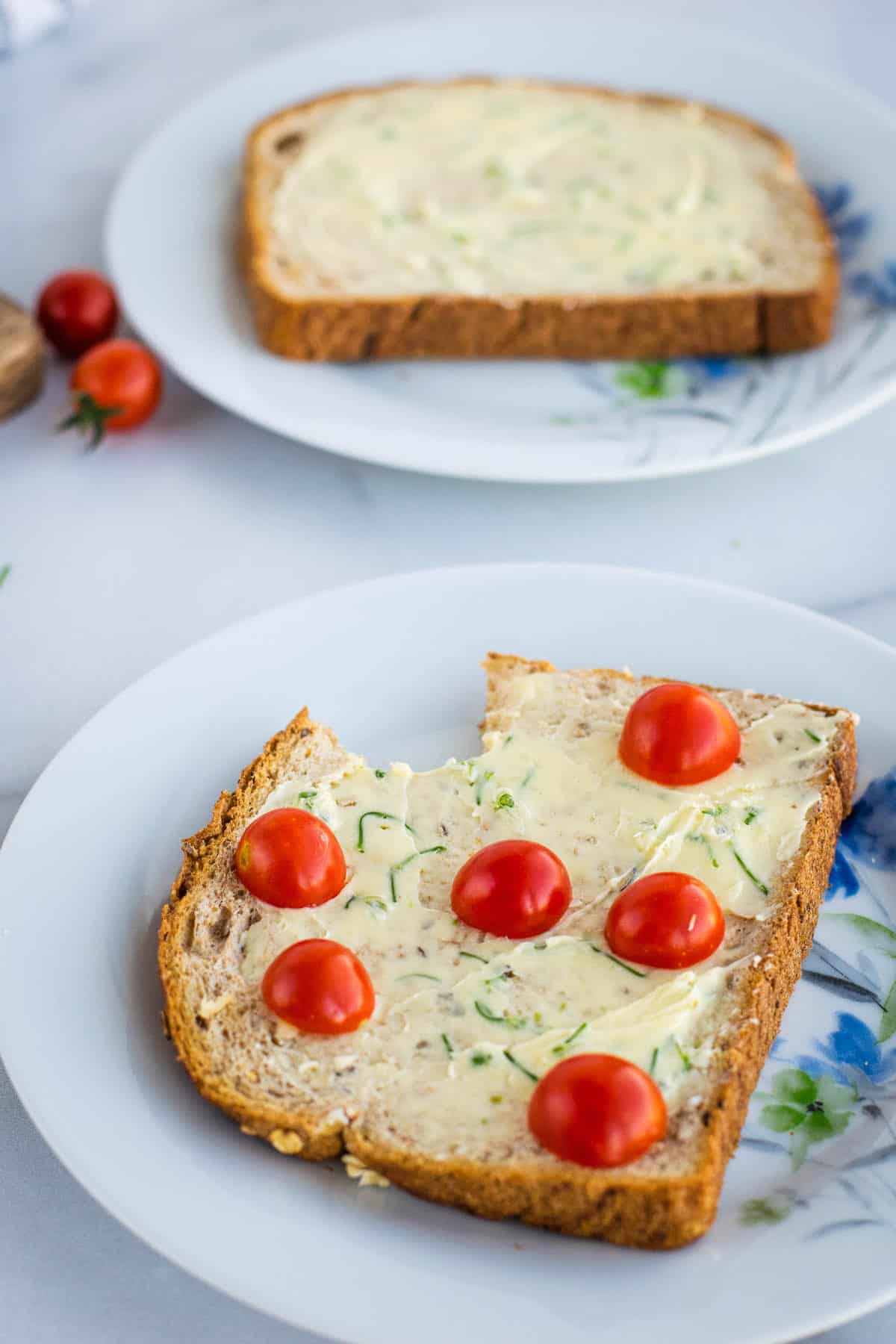 two pieces of toast on small plates with chive blossom butter and cherry tomatoes.