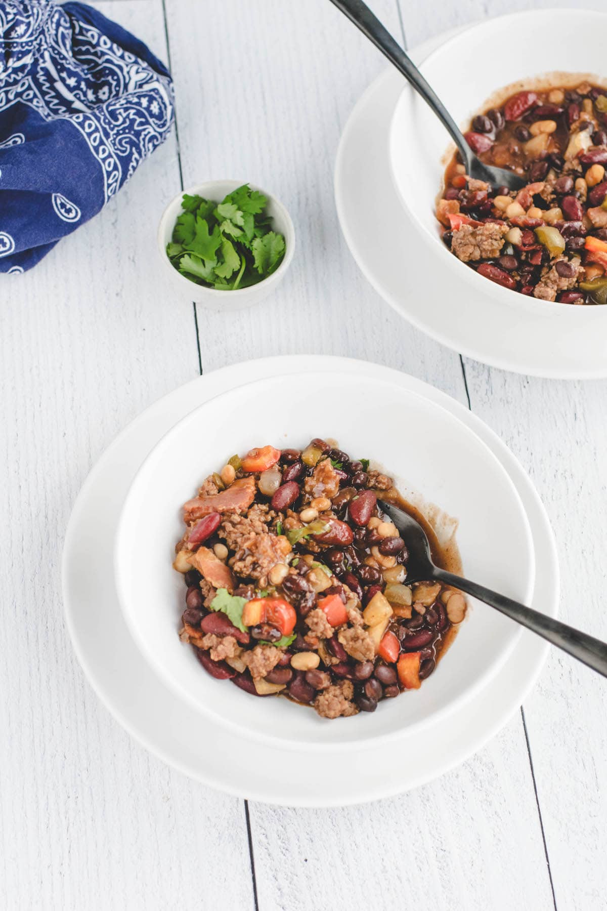 two white bowls with cowboy beans and small bowl of cilantro.