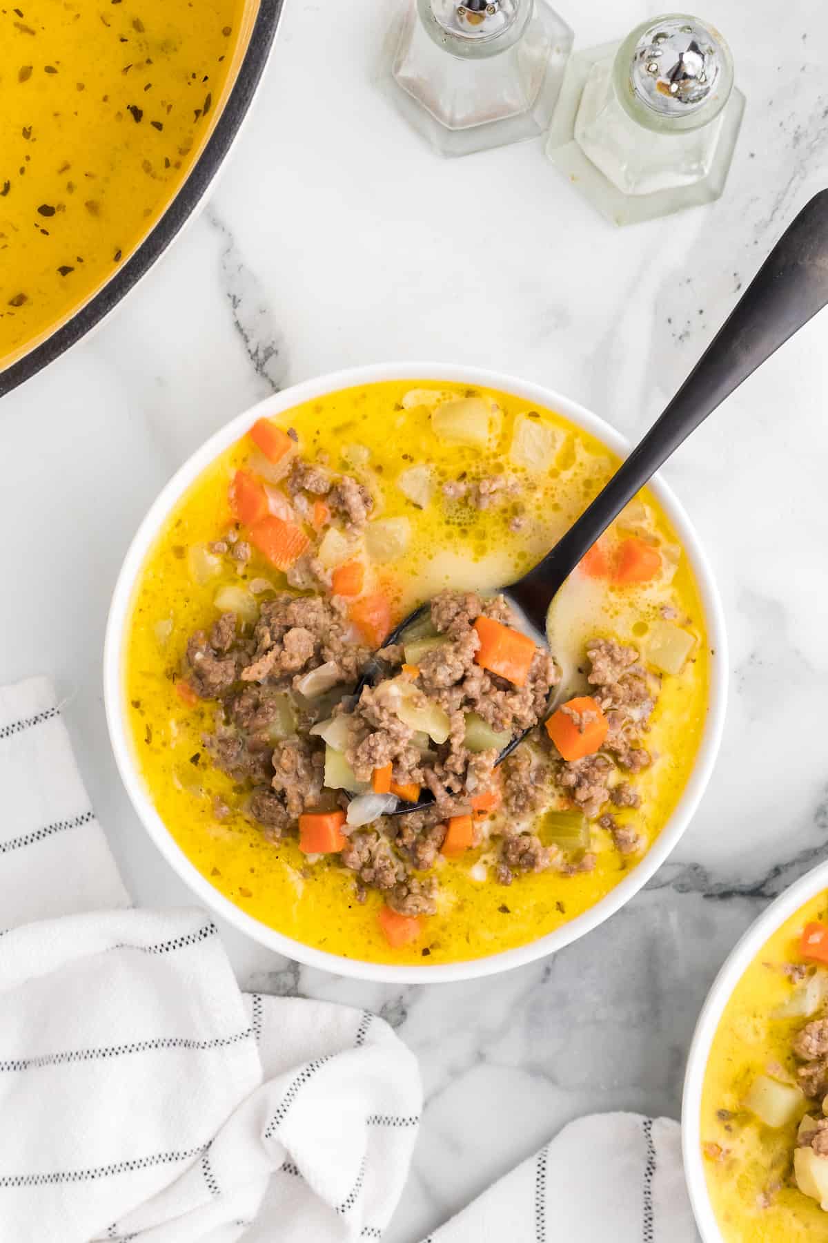 white bowl of healthy cheeseburger soup with a black spoon showing texture. 