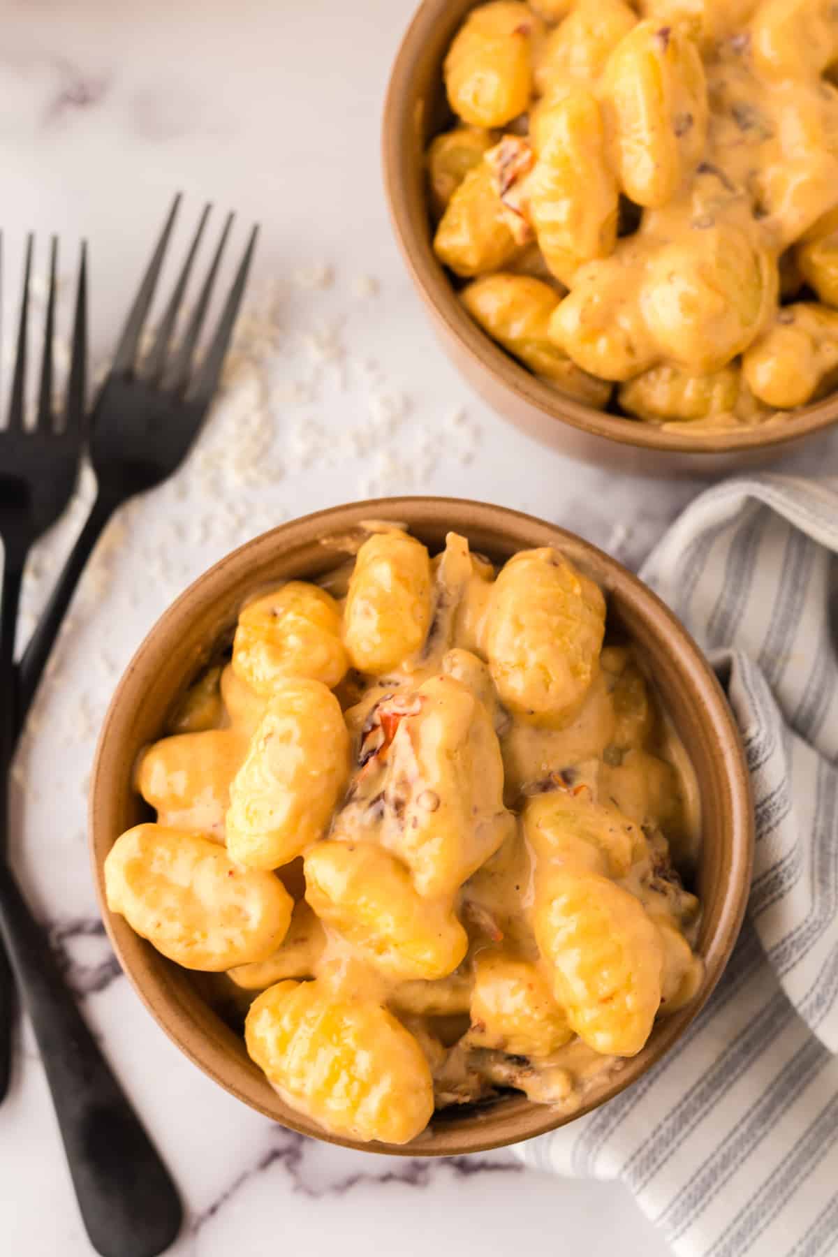two small bowls of creamy gnocchi with black forks to the side. 
