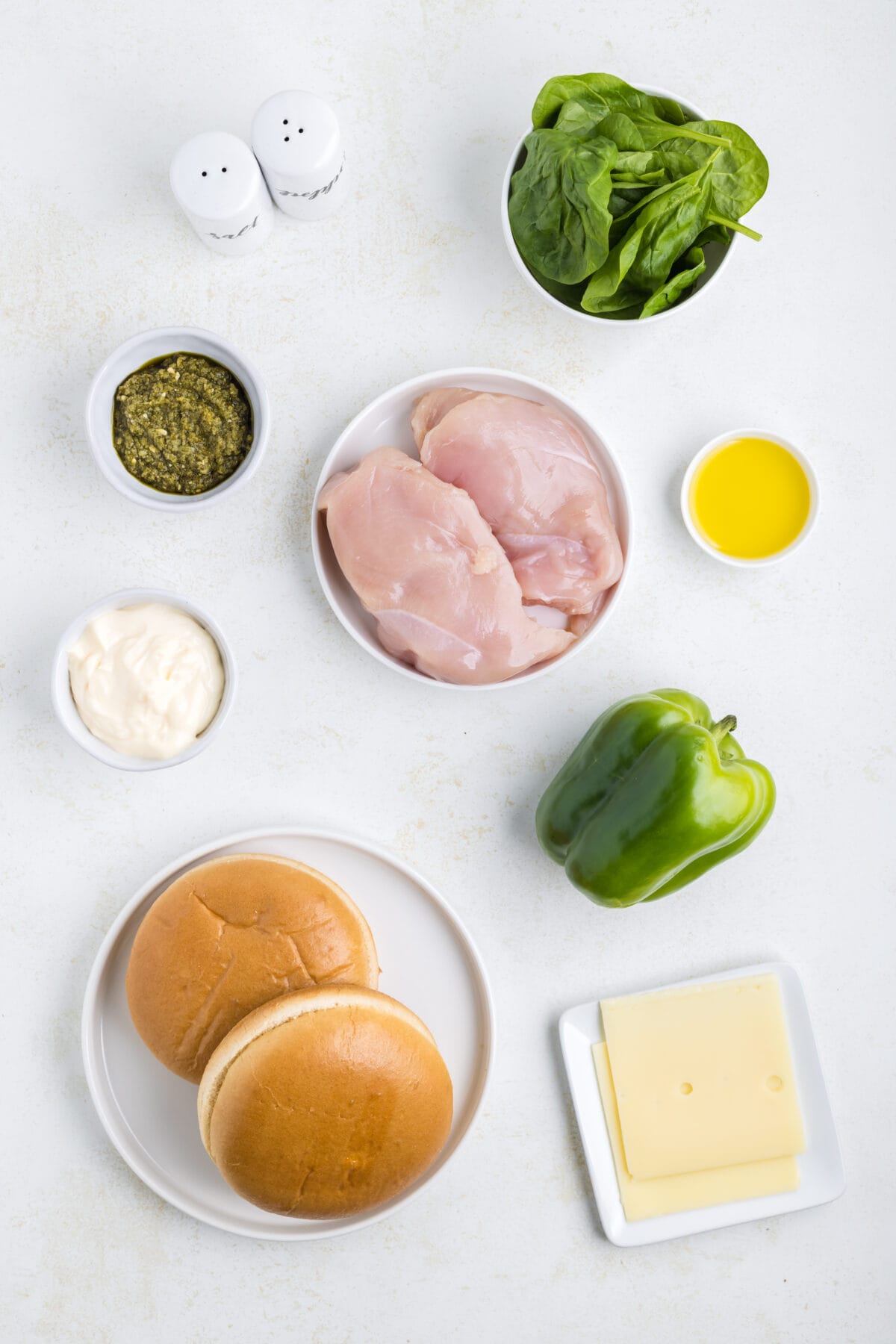 Ingredients used for the grilled chicken sandwich with pesto may in small bowls and plates.