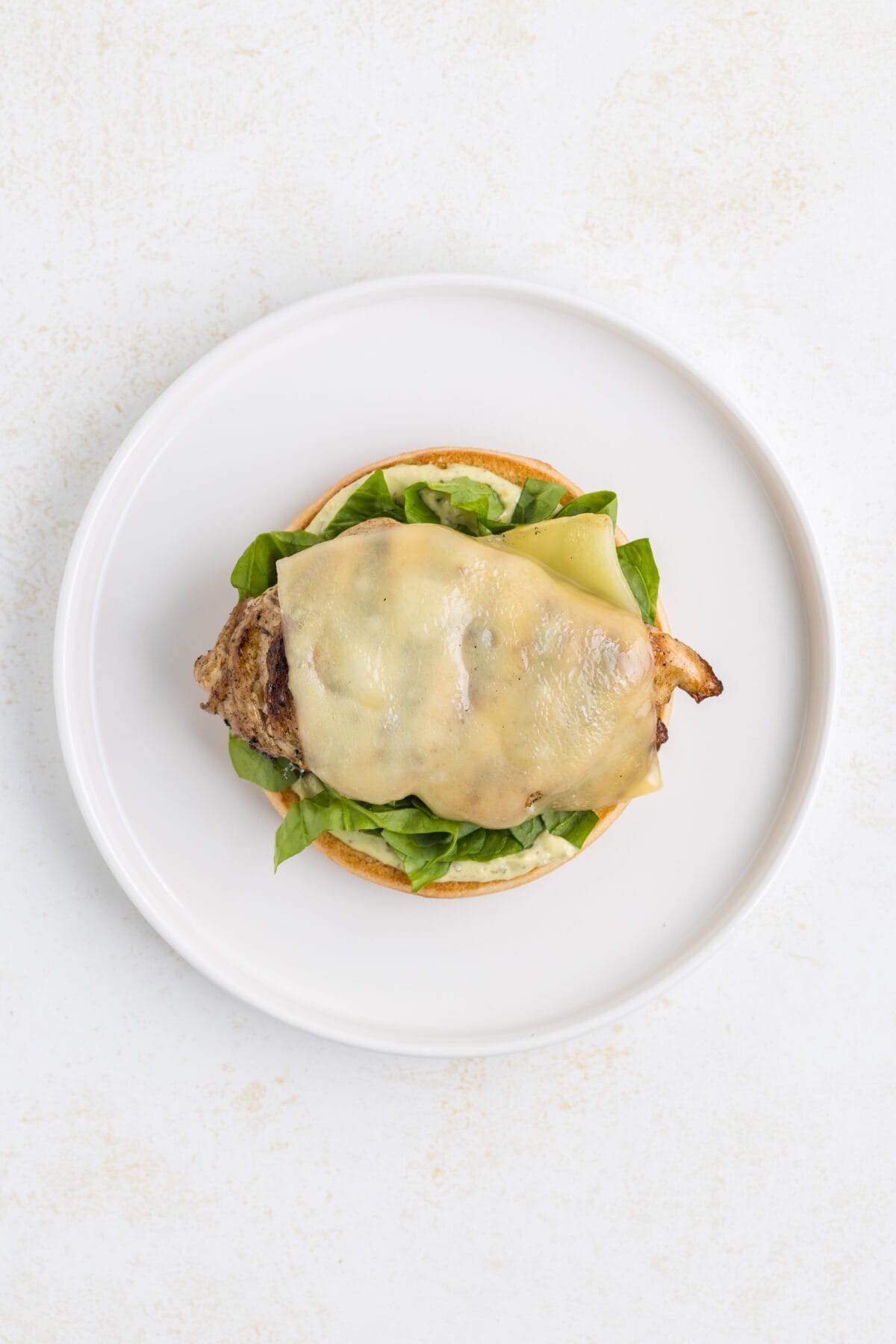 grilled chicken breast with melted Swiss cheese on top on a bottom half of a brioche bun.