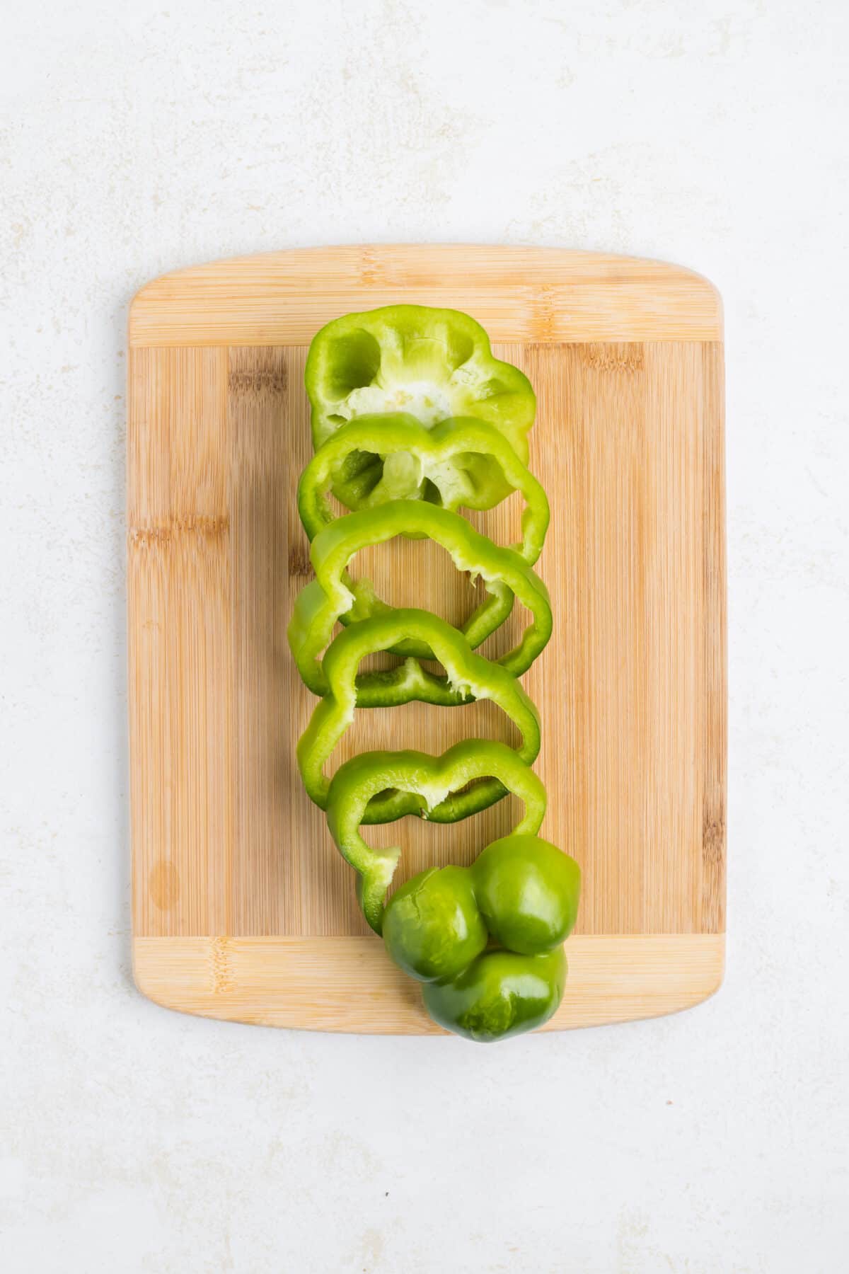 slicing the green bell peppers on a wooden cutting board.