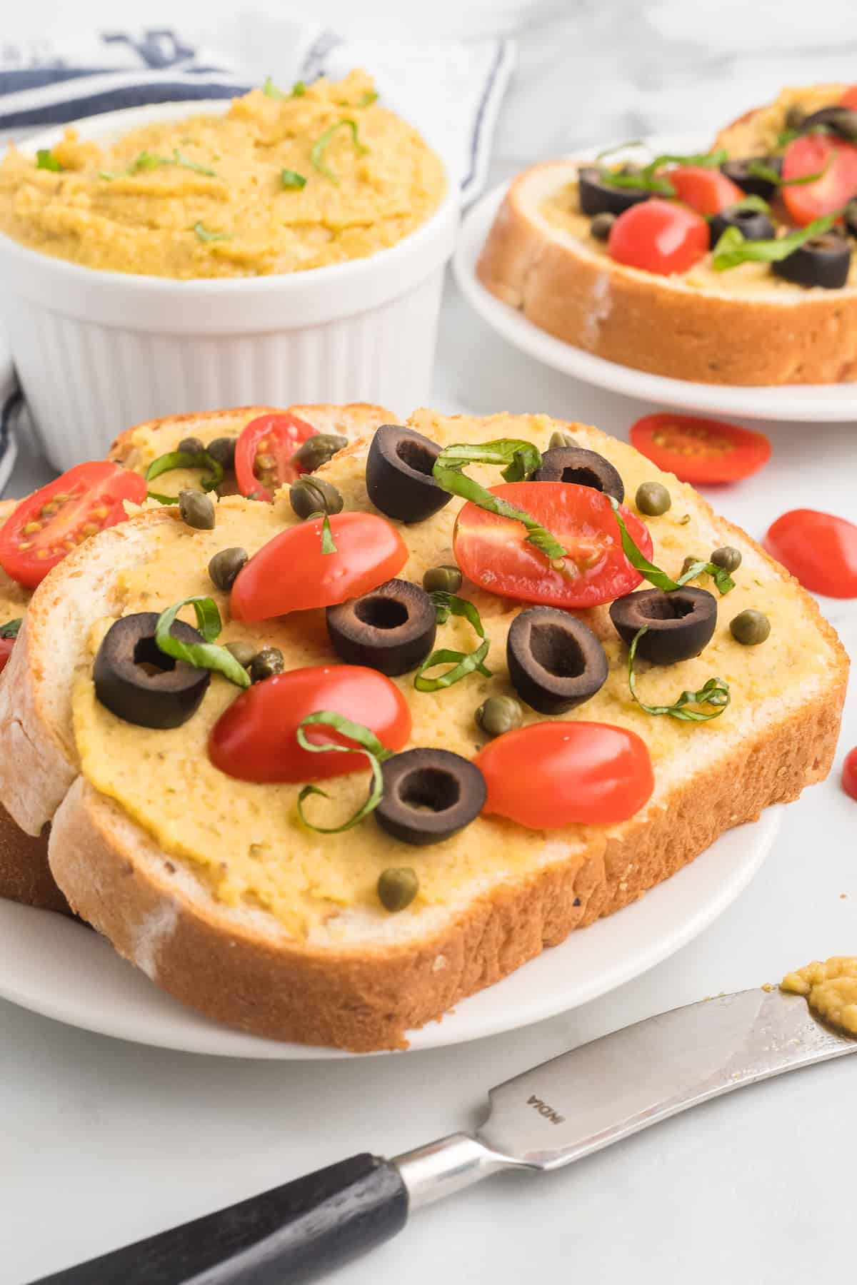 fresh garlic hummus spread over bread and topped with olives, tomatoes, and basil.