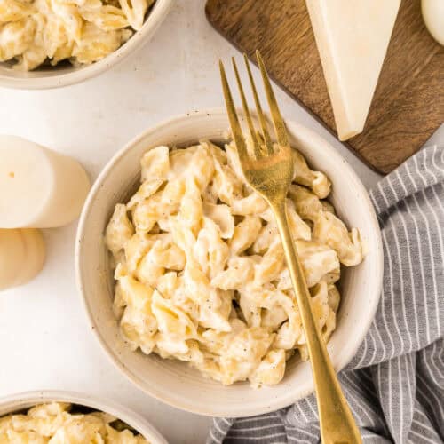 three white bowls of white cheddar Mac and cheese with a gold fork resting on top of one.