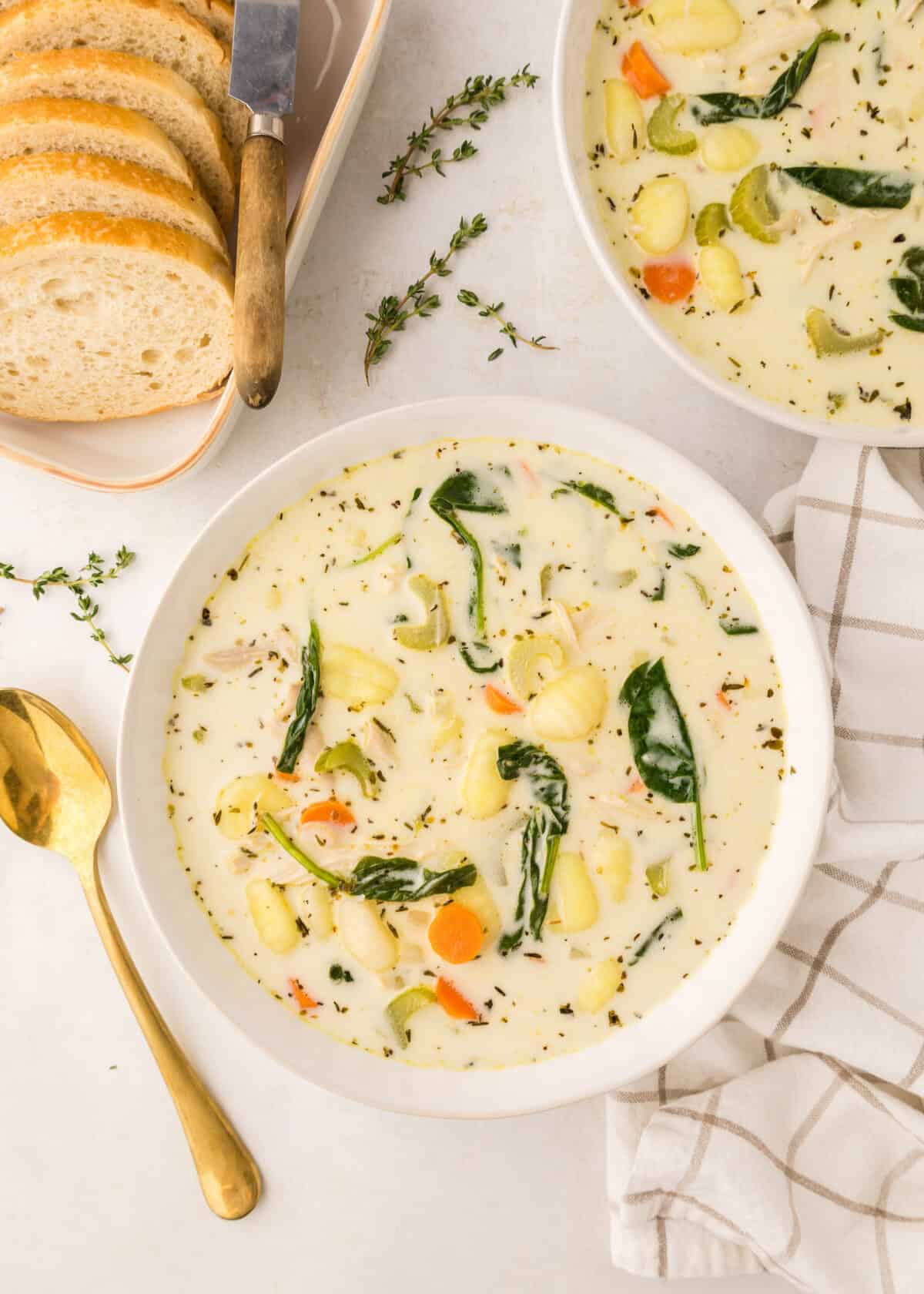 two white bowls of homemade chicken gnocchi soup with slices of homemade bread to the side. 