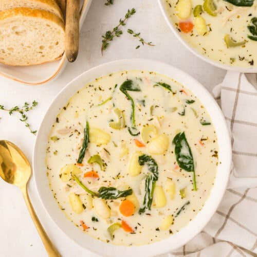 two white bowls of homemade chicken gnocchi soup with slices of homemade bread to the side.