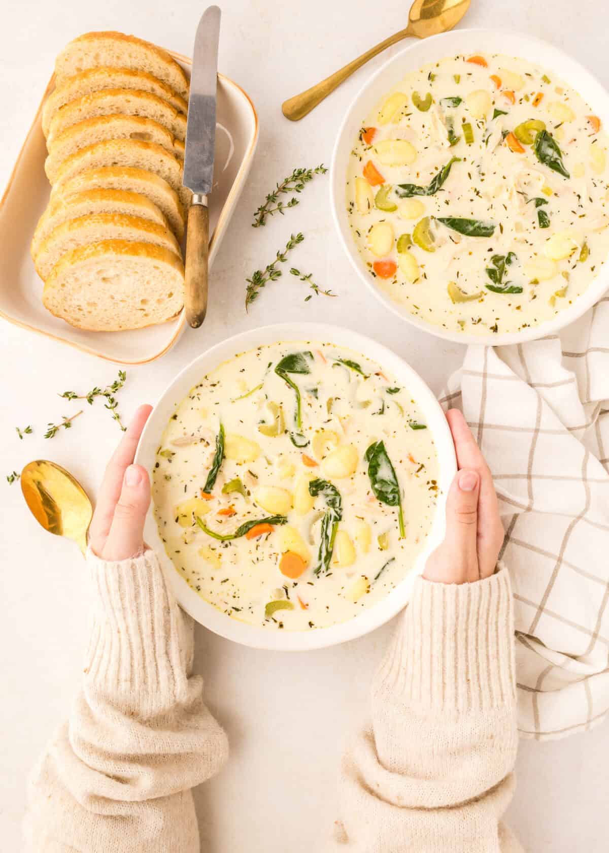 two white bowls of creamy chicken gnocchi with plate of slices of fresh bread to the side. 