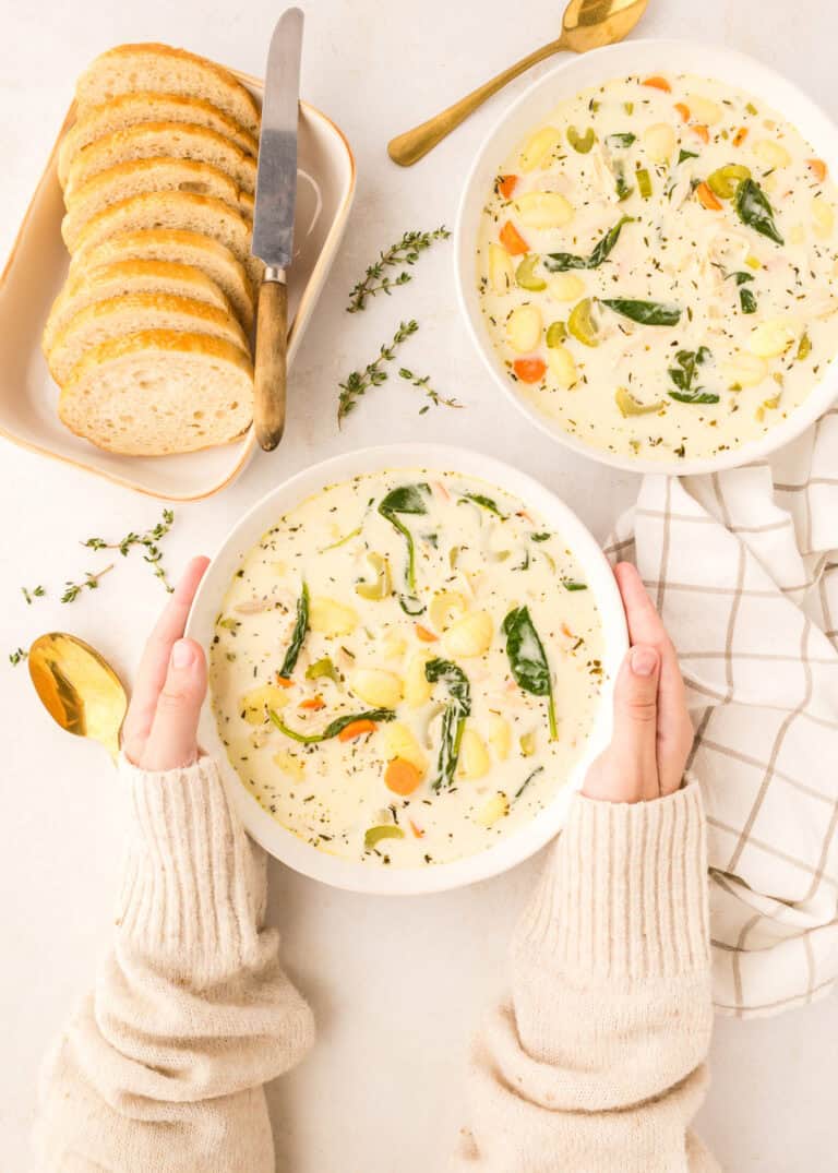 two white bowls of creamy chicken gnocchi with plate of slices of fresh bread to the side.