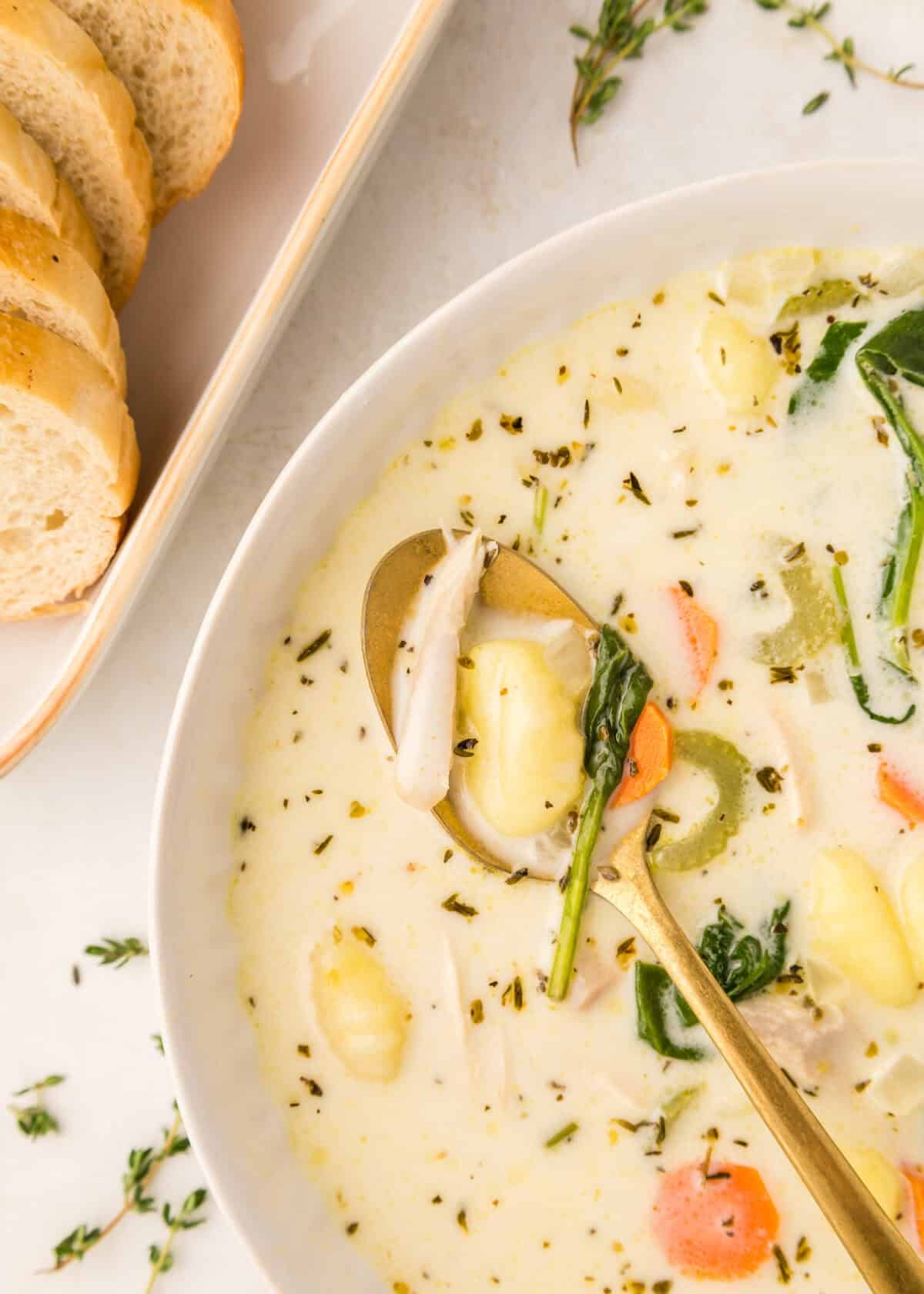 white bowl closeup of creamy chicken gnocchi soup with gold spoon. 