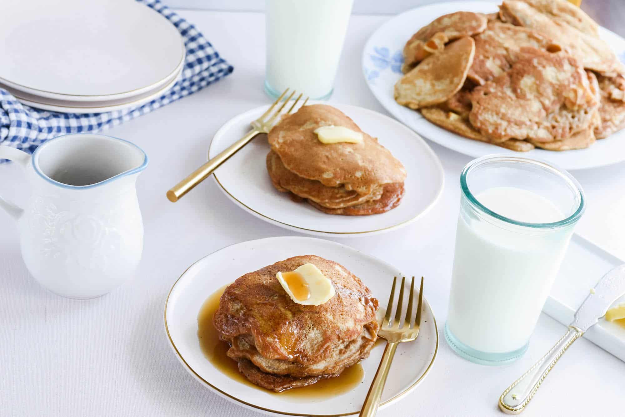 two white plates stacked with apple cinnamon sourdough pancakes and butter with drizzle of maple syrup.