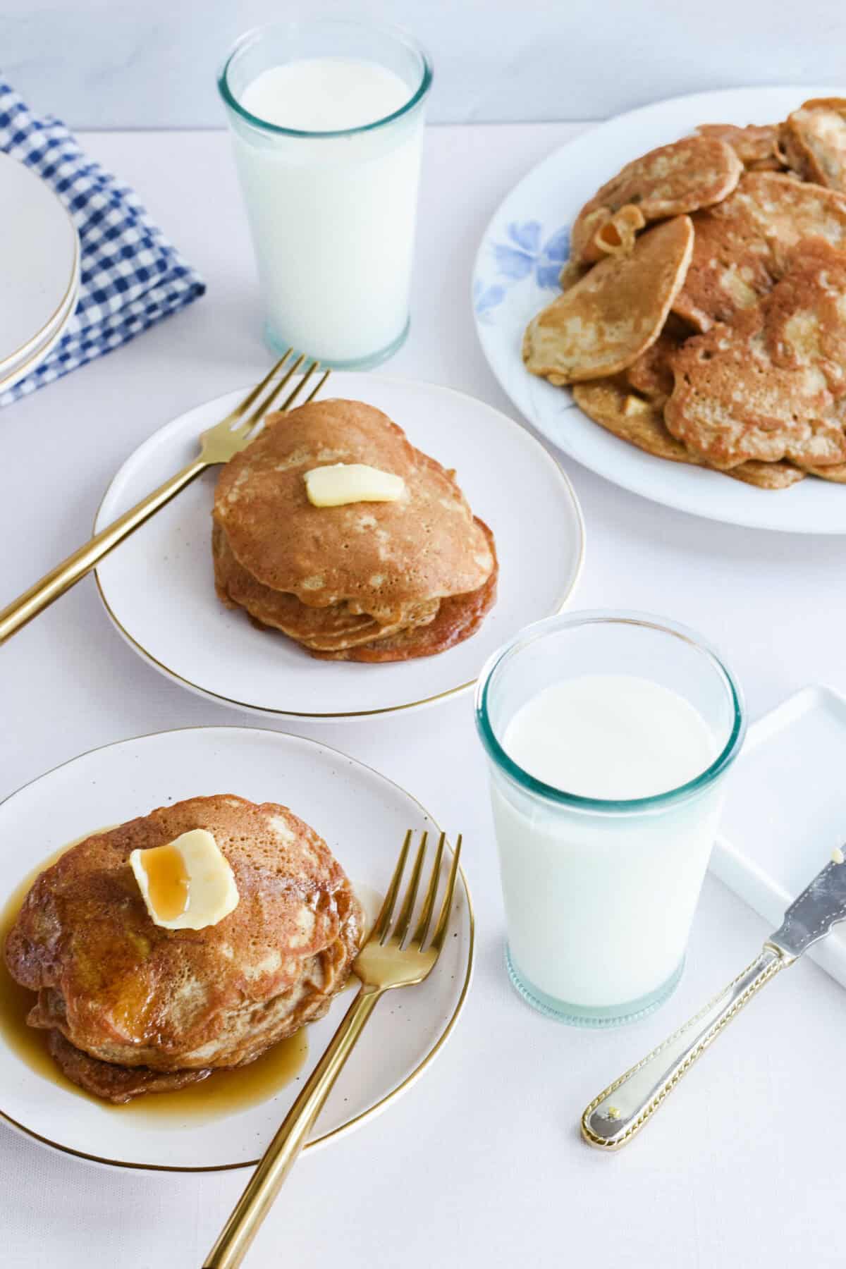 two white plates stacked with apple cinnamon sourdough pancakes and butter with drizzle of maple syrup. 