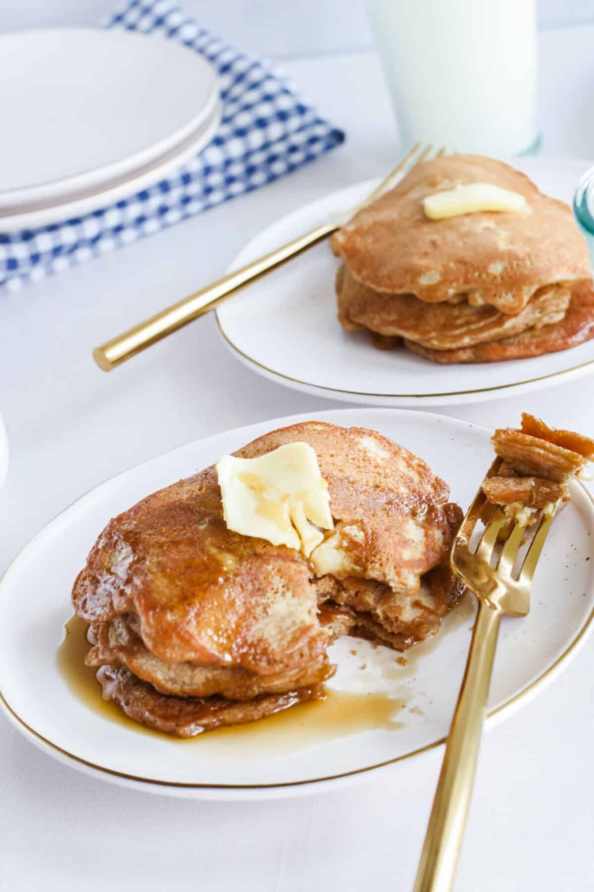 gold fork with a bite size sourdough pancake. with another plate and napkins to the back. 