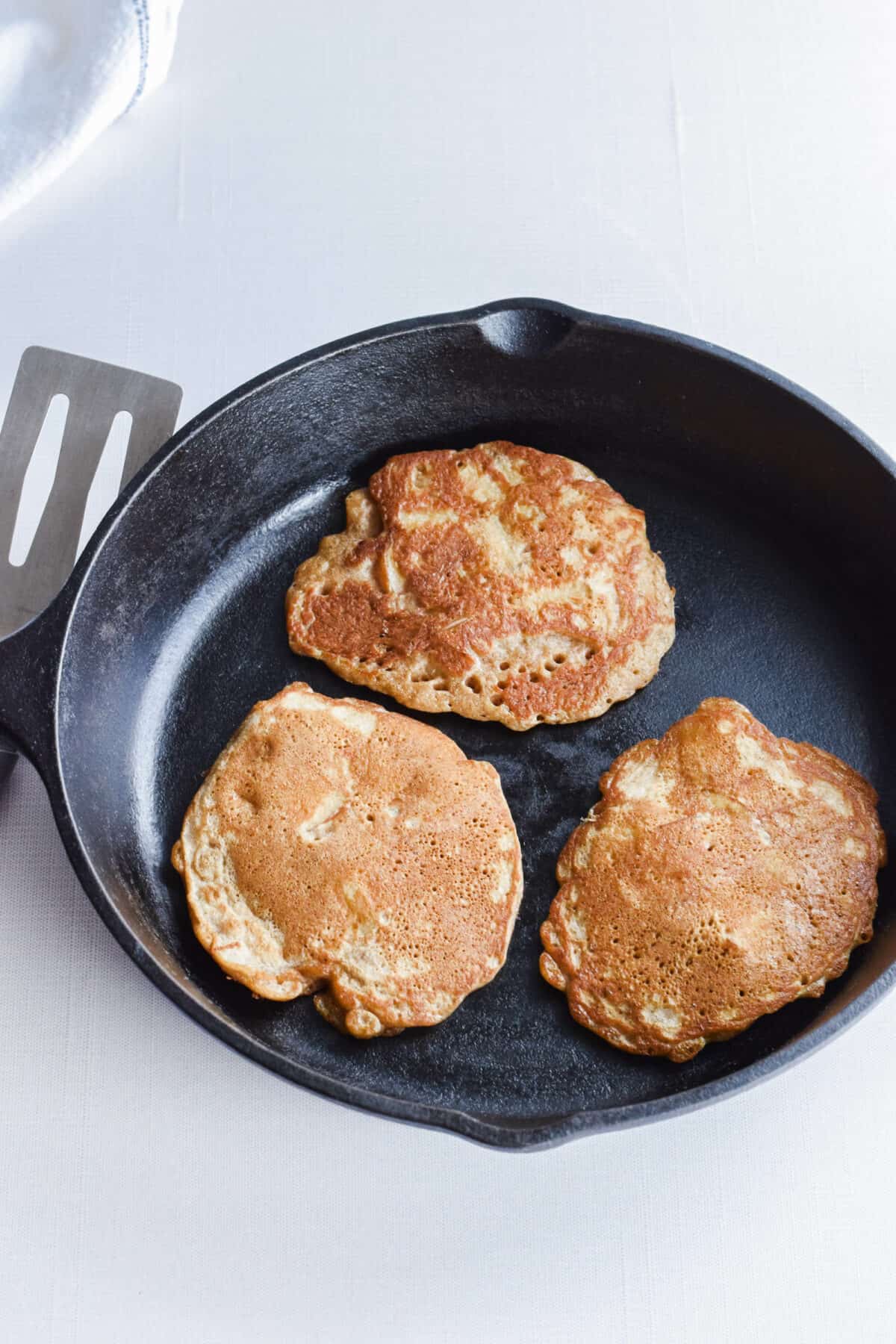 apple cinnamon sourdough pancakes cooked on one side in a cast iron skillet. 