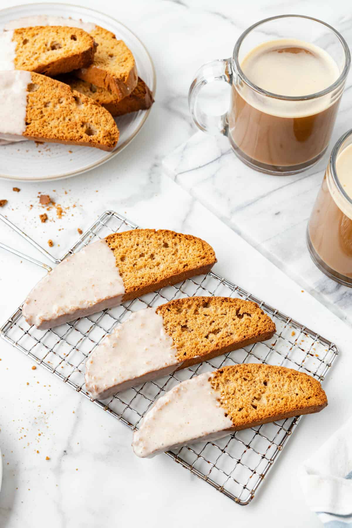 3 pumpkin spice biscottis on a wire rack with 2 mugs of coffee to the side. 