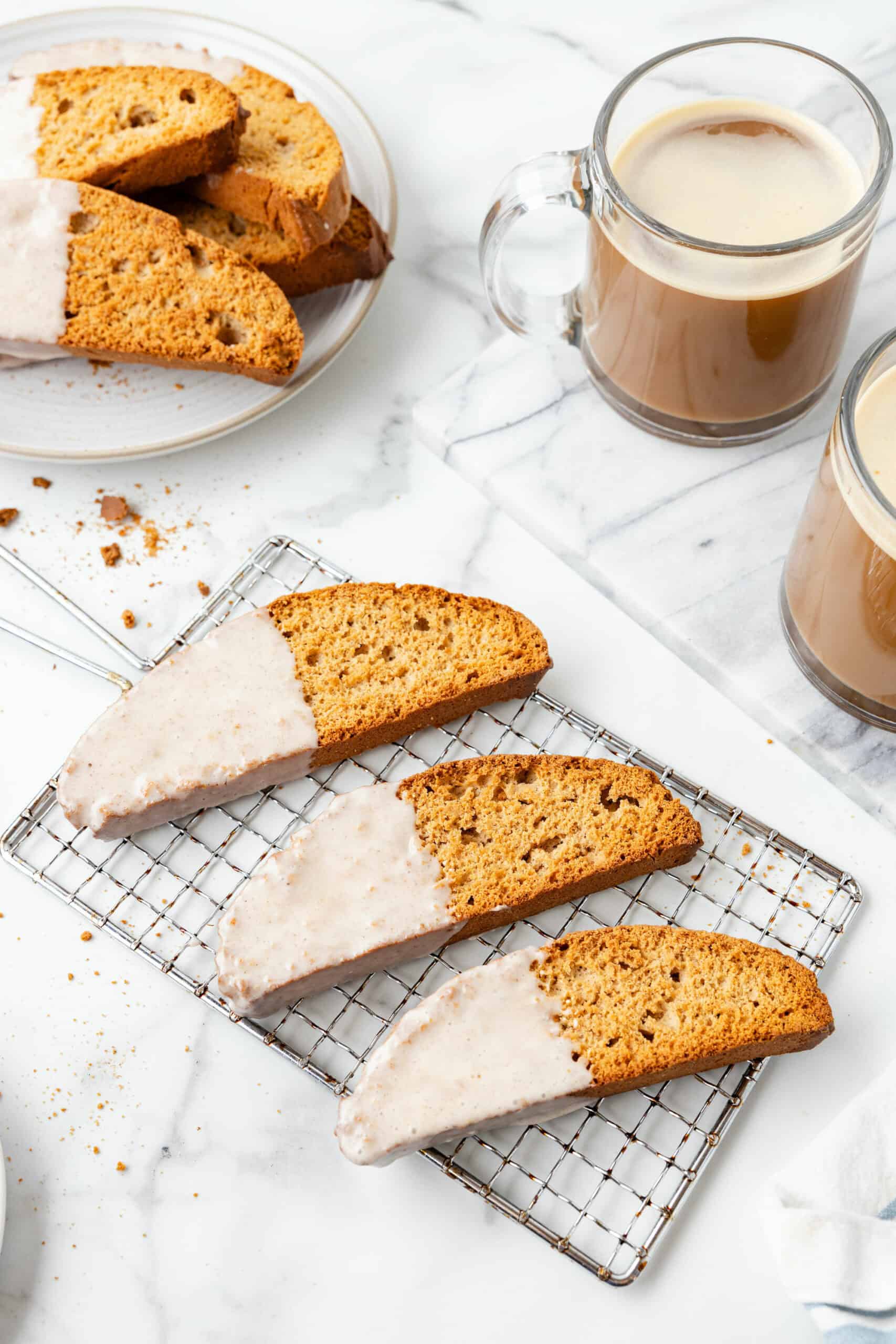 3 pumpkin spice biscottis on a wire rack with 2 mugs of coffee to the side.