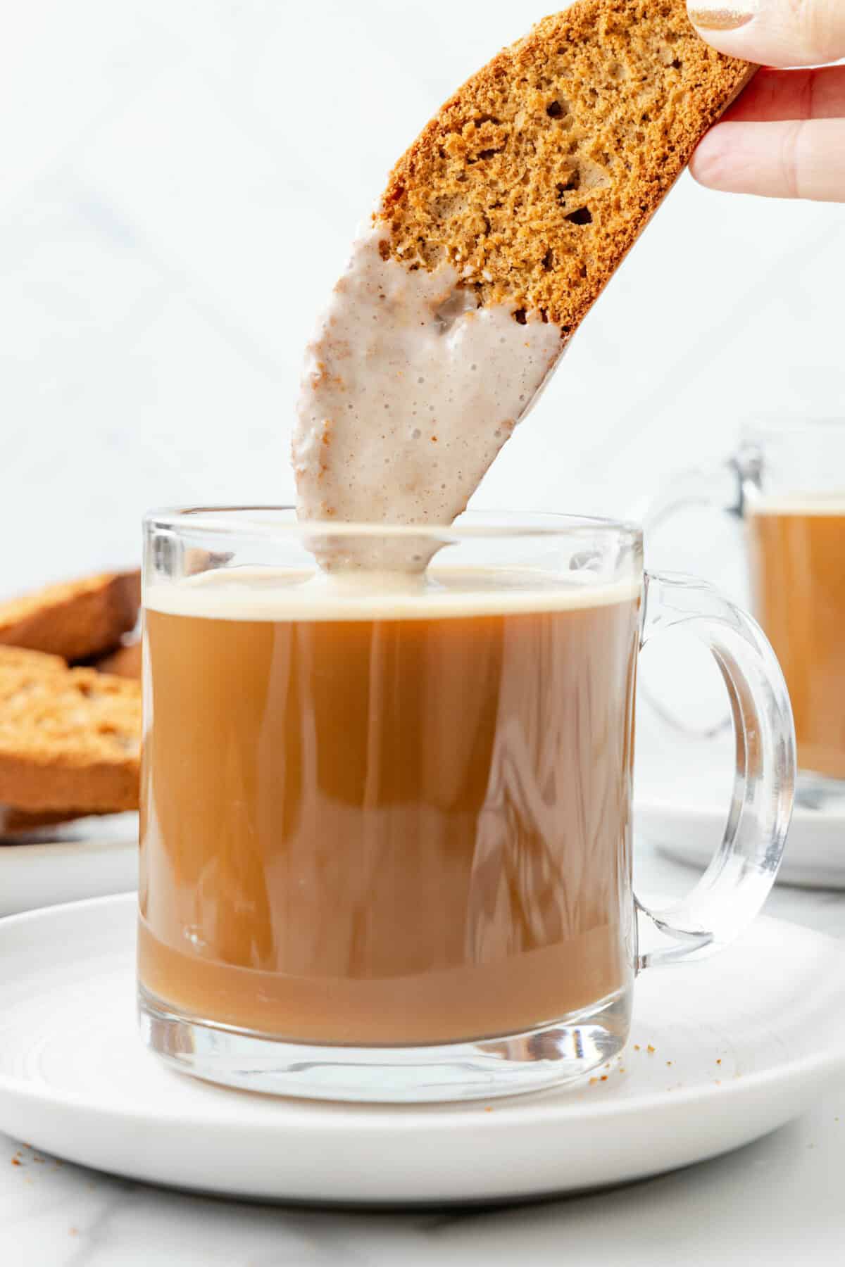 a mug of coffee with a pumpkin spice biscotti being dunked inside.