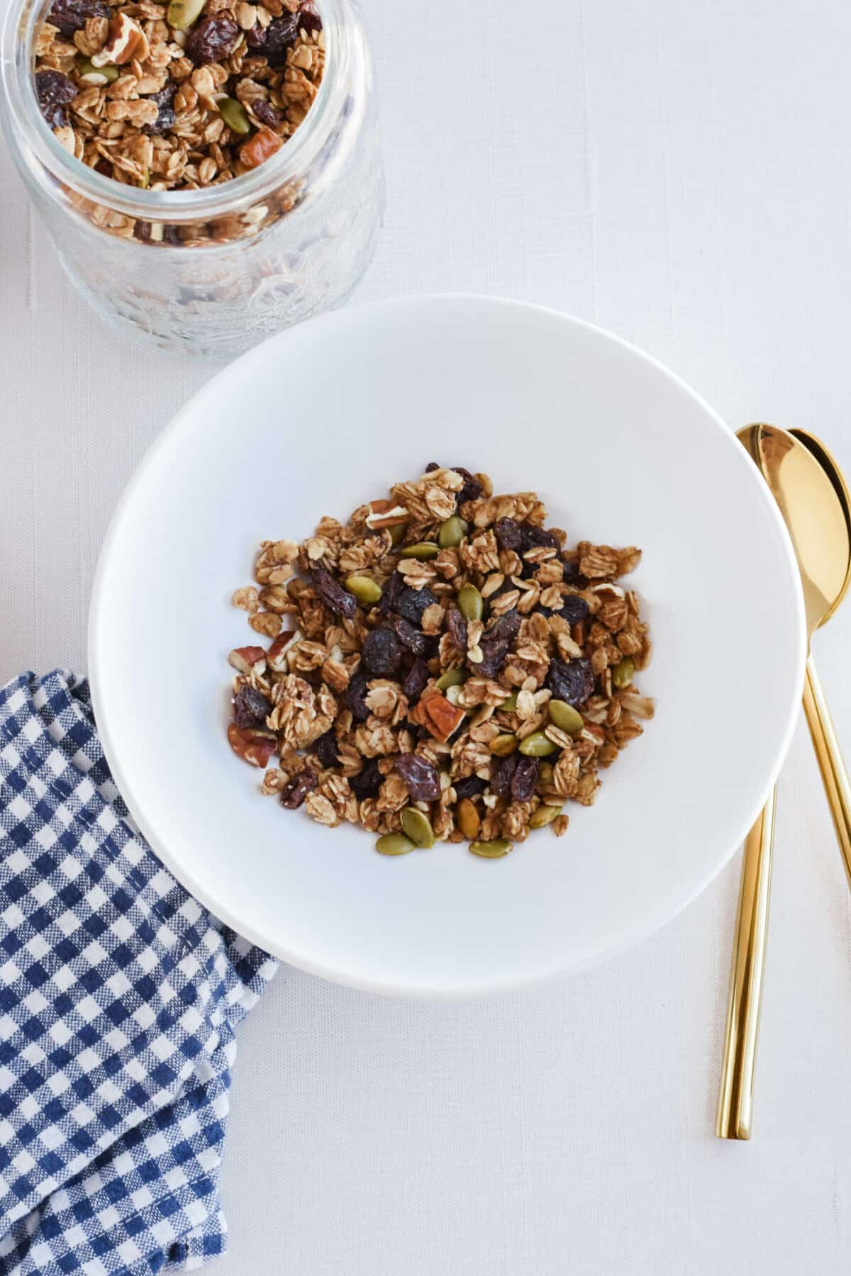 white bowl with pumpkin spice sourdough granola and gold spoons to the side. 