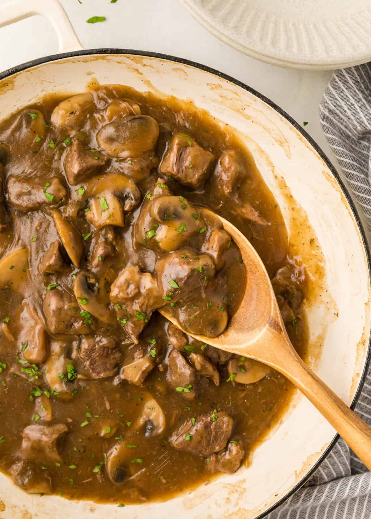 beef tips gravy with mushrooms in a dutch oven with a wooden spoon. 