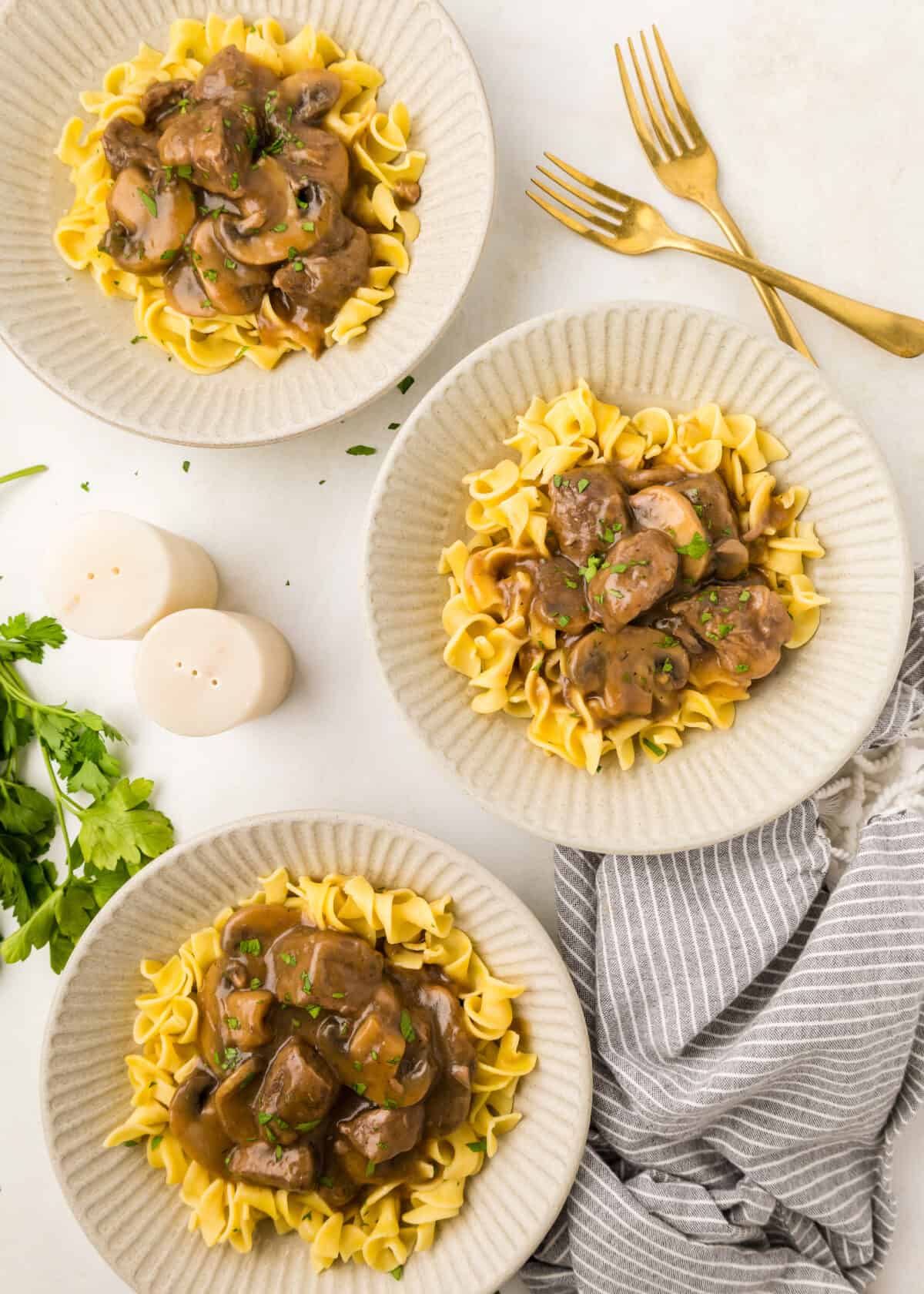 three plates with beef tip gravy over egg noodles. 