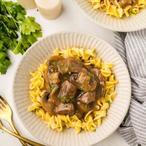 two plates with beef tip gravy over egg noodles.