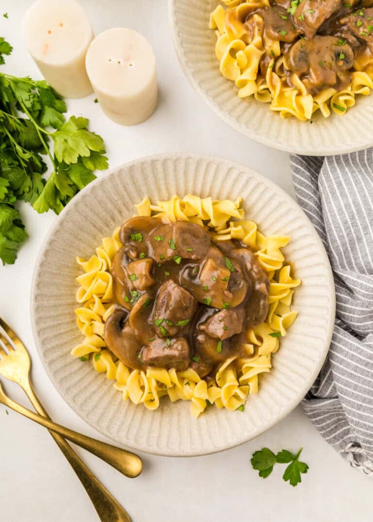 two plates with beef tip gravy over egg noodles.