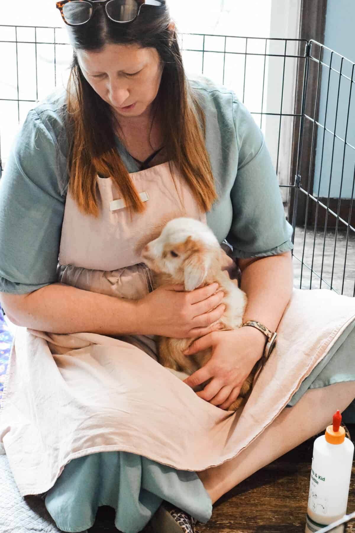 Mary holding a young goat while sitting on the floor. 