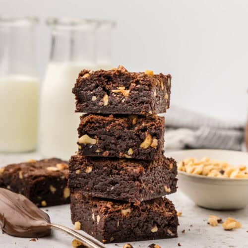 Slices of Nutella brownies stacked on top of each other with a spoon full of Nutella to the side.