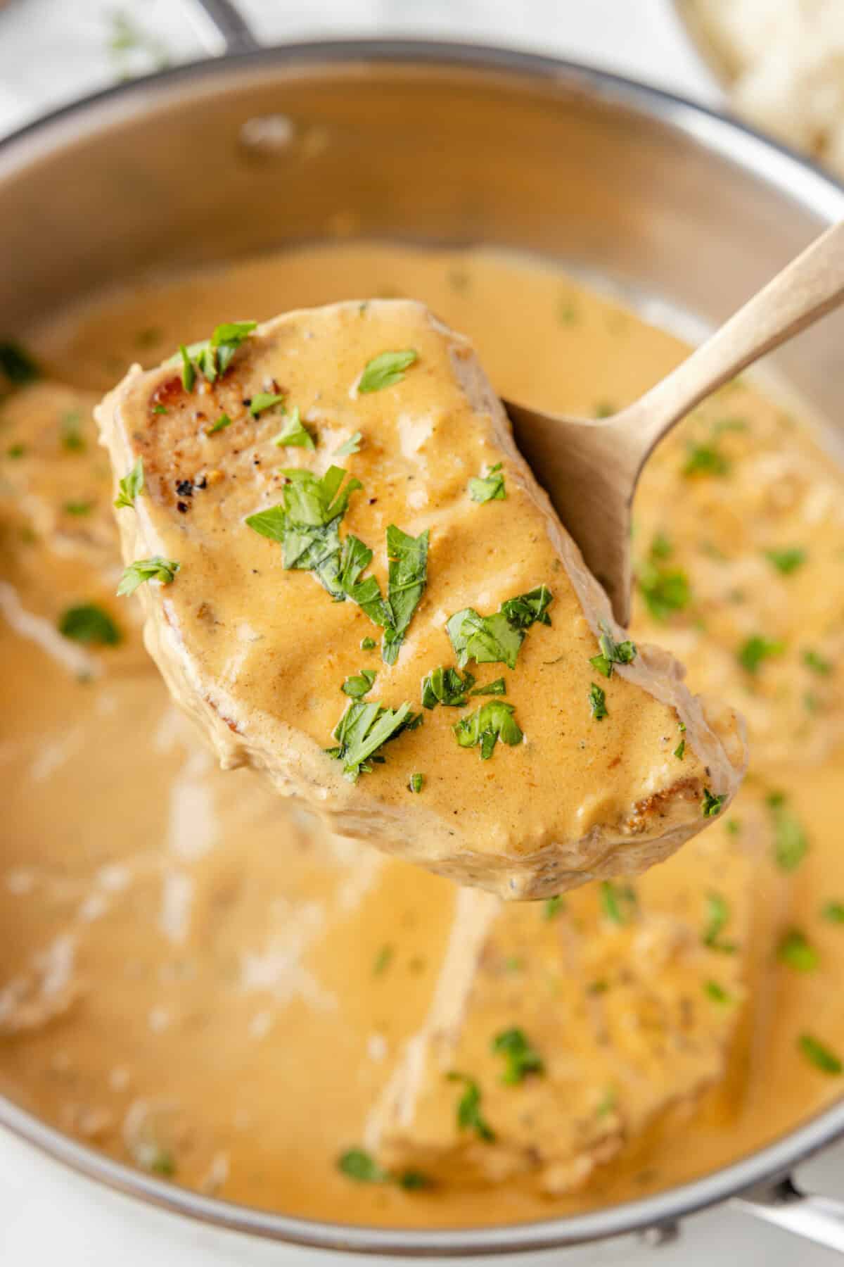 stainless steel skillet with creamy pork chops and spatula lifting one out of the pan. 