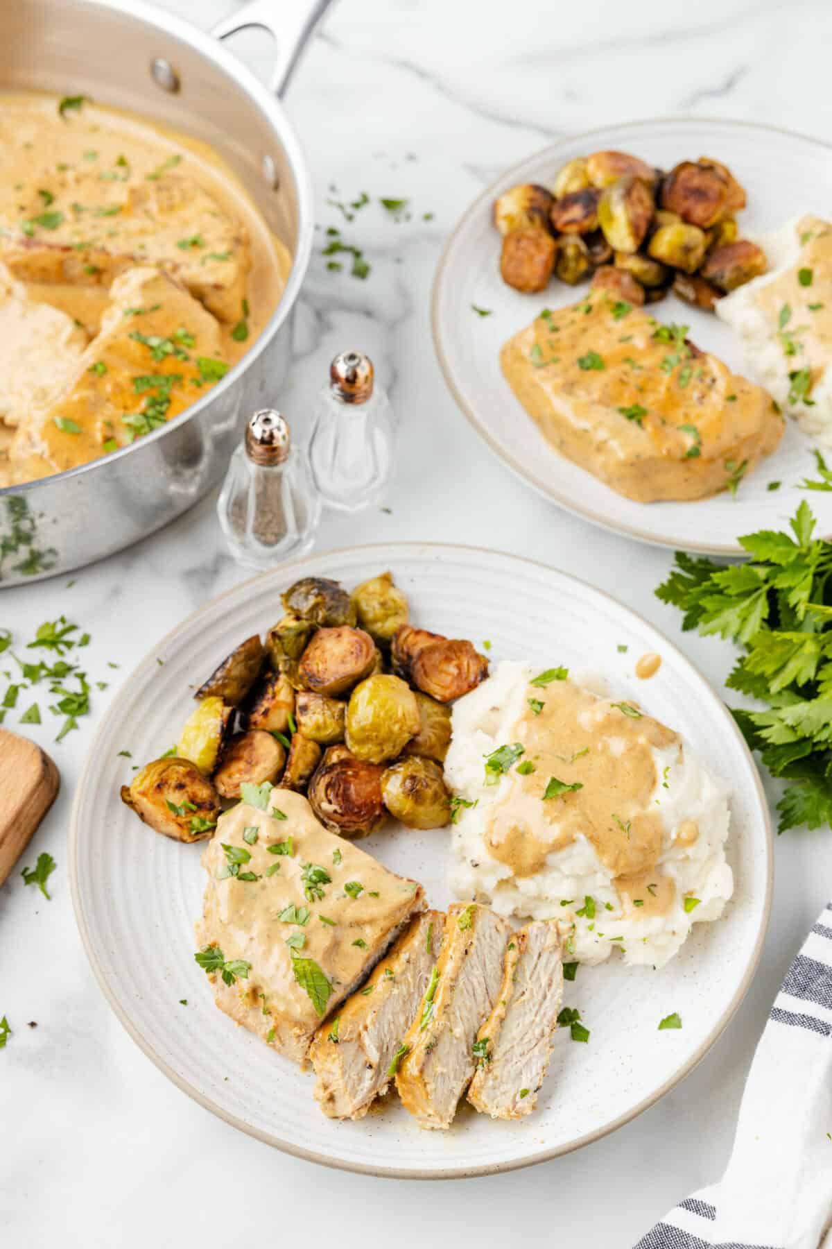 white plates of creamy pork chops with mashed potatoes and gravy and roasted Brussels sprouts. 