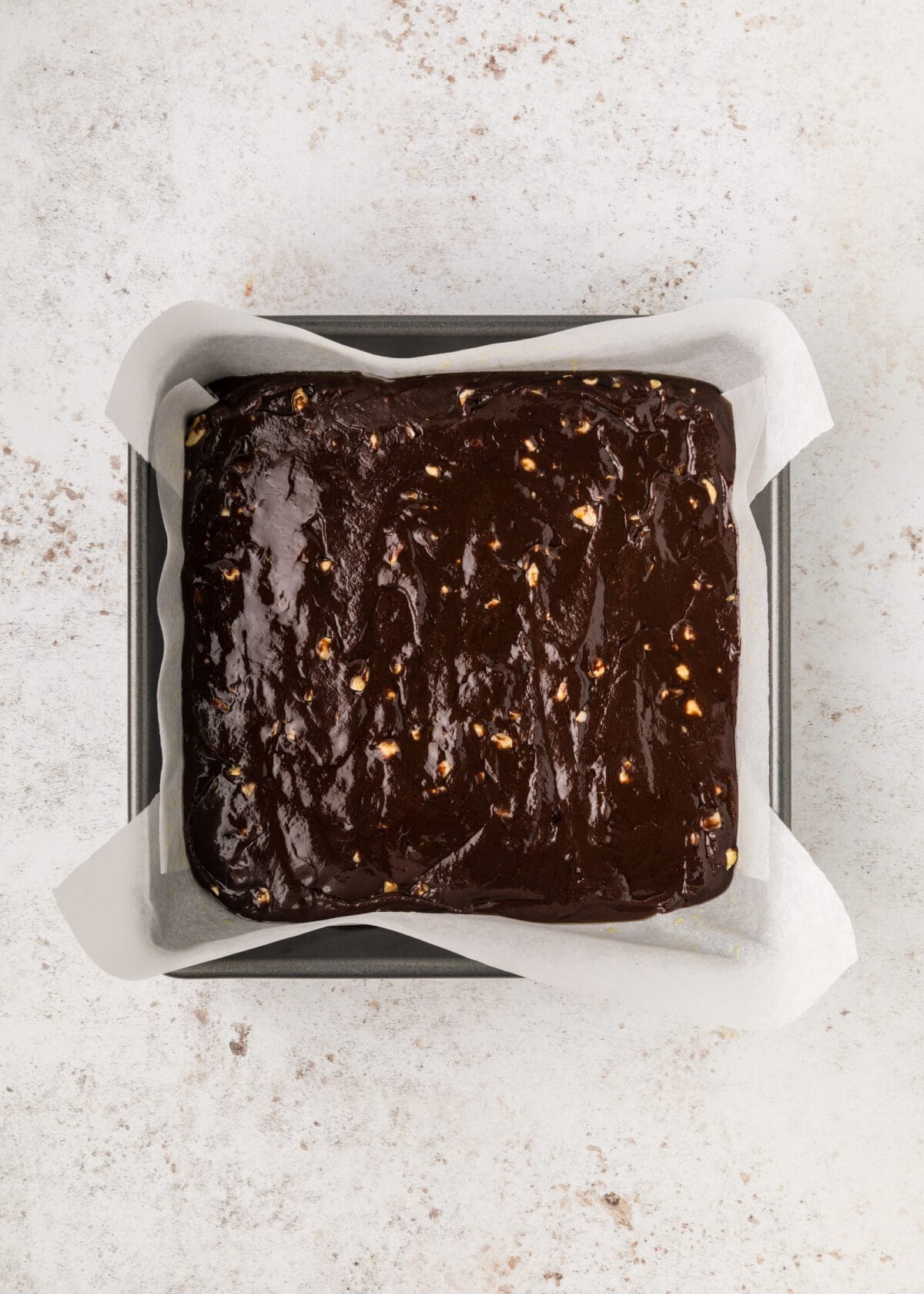 nutella brownie batter added to a parchment paper lined baking pan. 