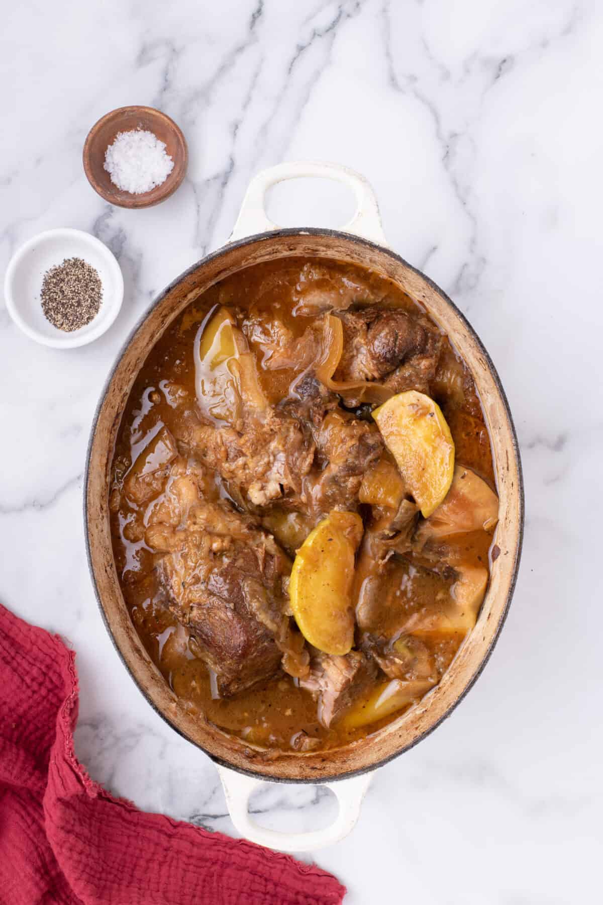 white dutch oven with finished pork shoulder roast, onions, and apples. 