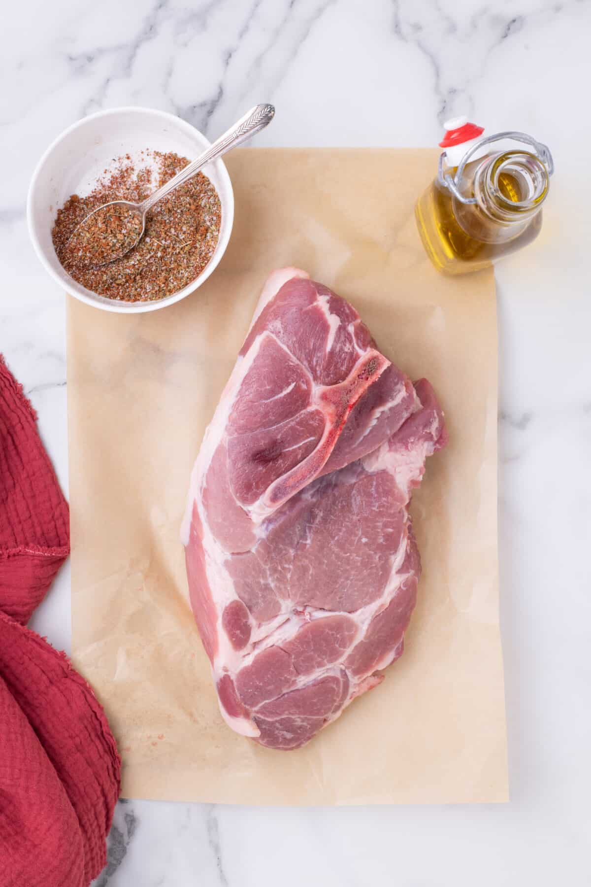 pork shoulder on a cutting board with seasonings in a small bowl to the side. 