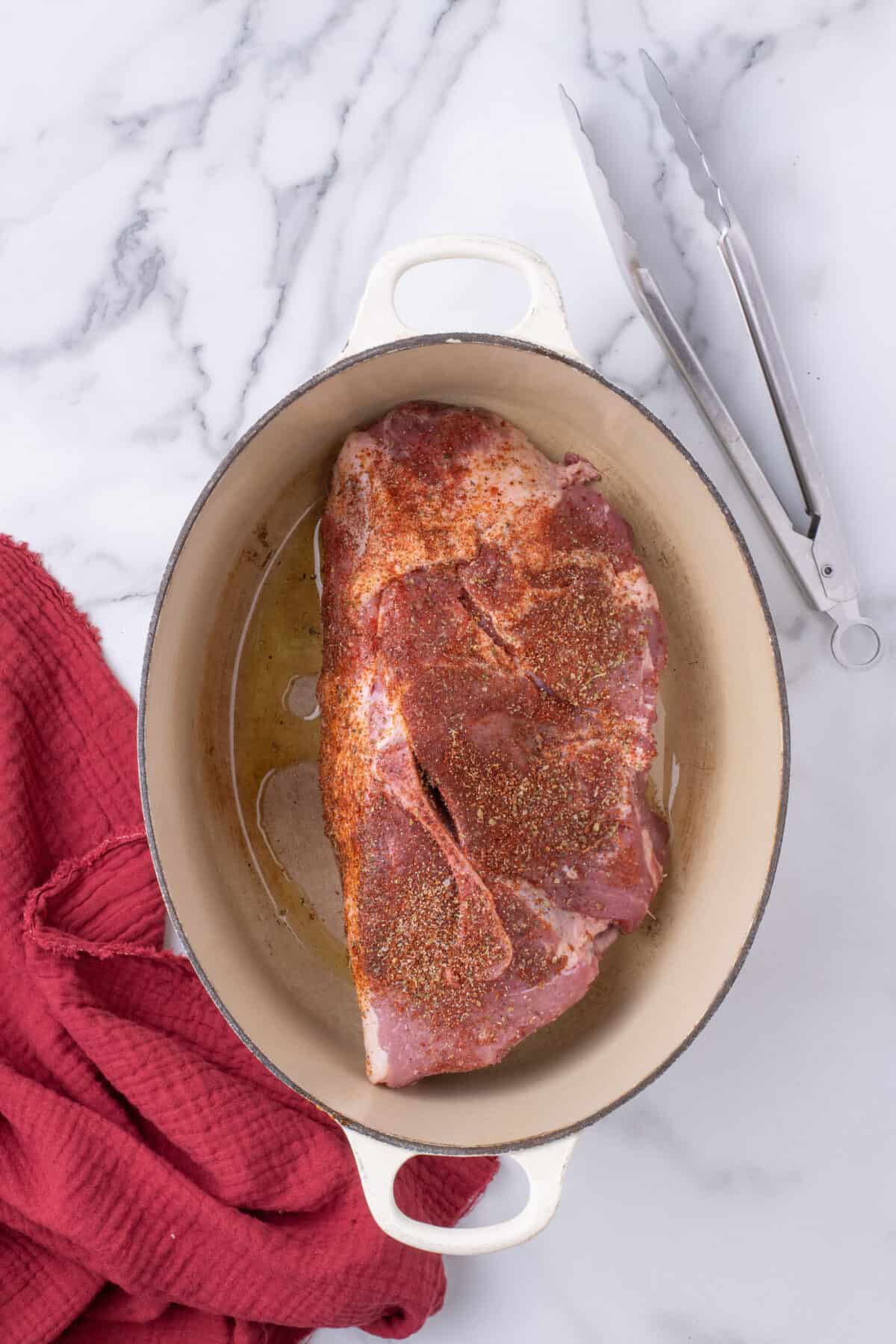 pork shoulder with seasoning rub inside of a dutch oven. 