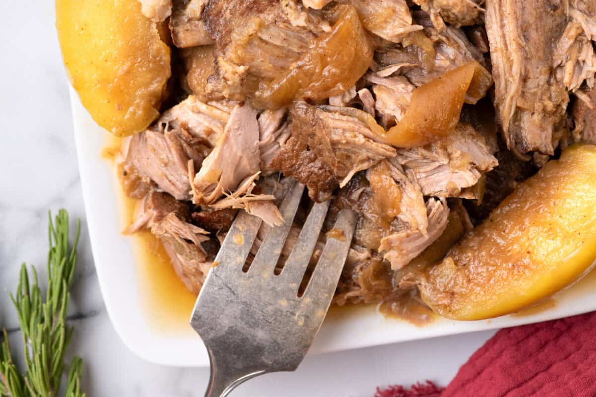 apple cider braised pork shoulder on a white platter with a fork. 