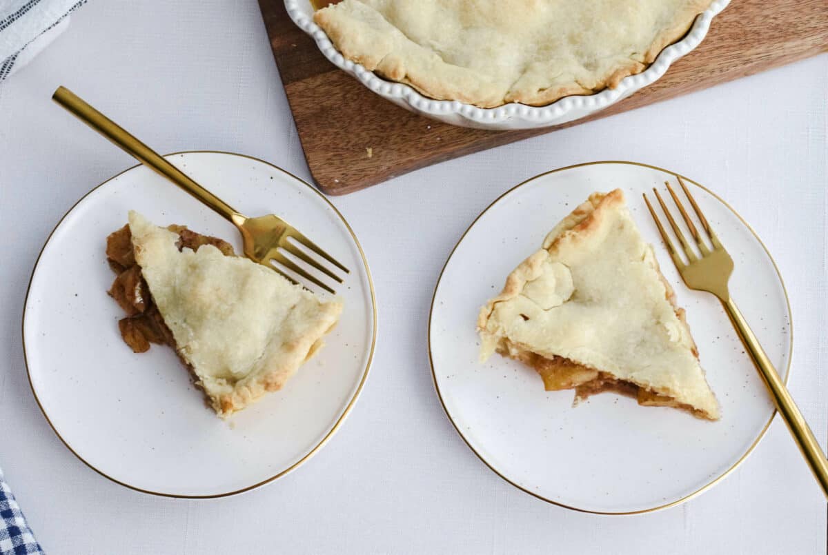 slices of apple pie on white dessert plates with gold forks.