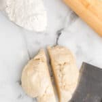 pie crust dough divided in half and a bench scraper to the side.