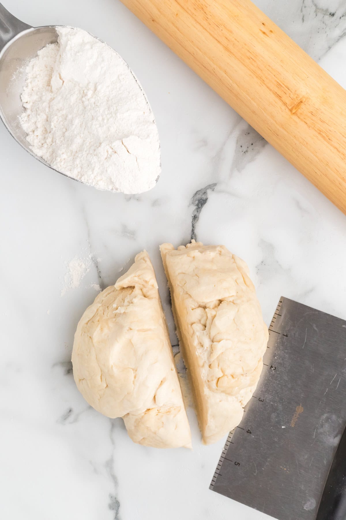 pie crust dough divided in half and a bench scraper to the side. 