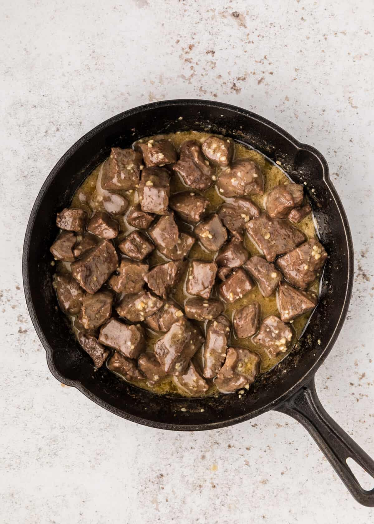 added the steak bites to the cast iron skillet with the melted butter and minced garlic. 