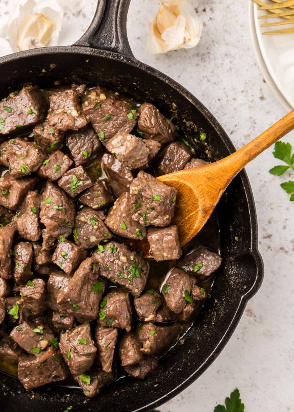 serving the finished garlic butter steak bites out of the cast iron skillet with a wooden spoon. 