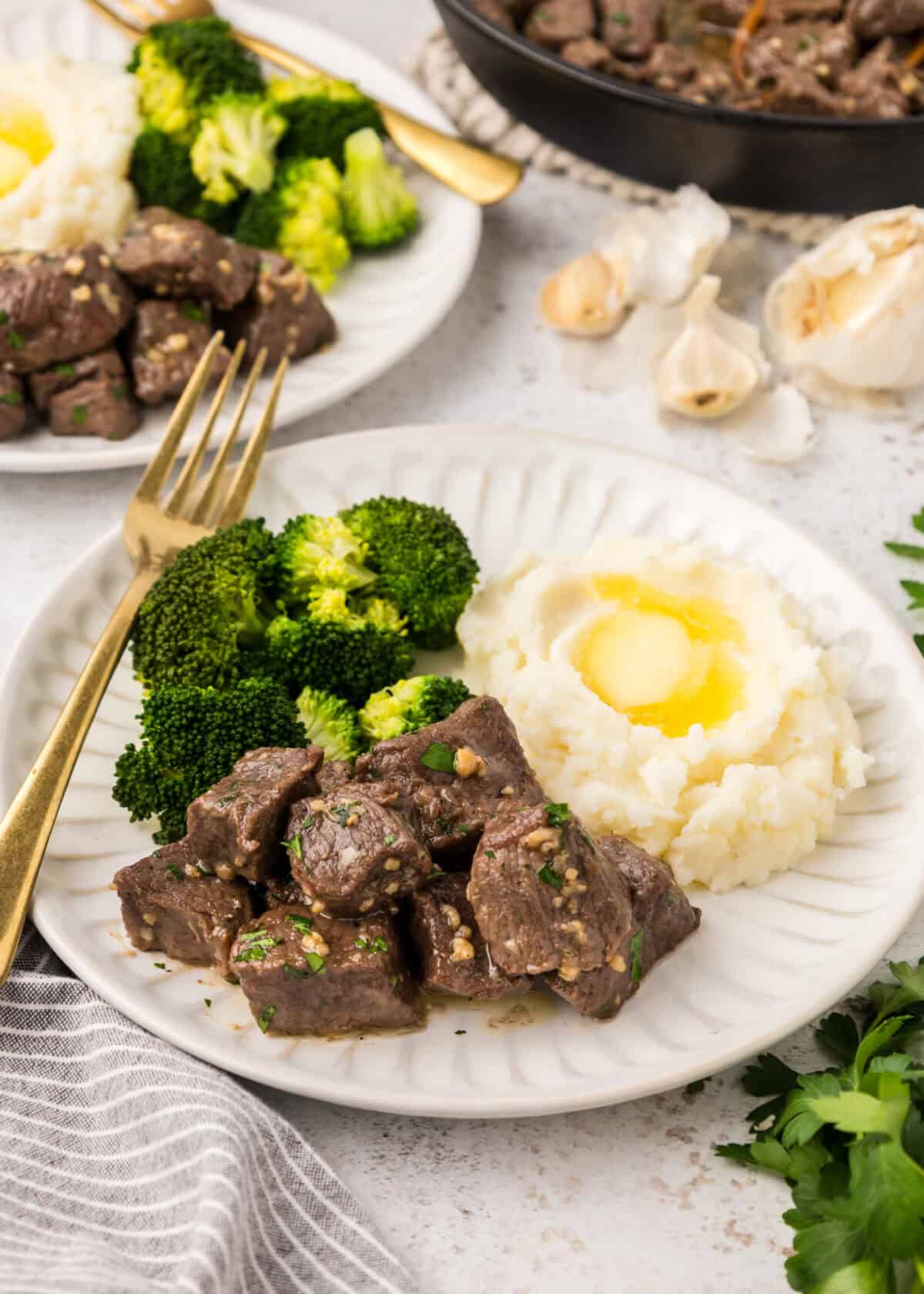 garlic butter steak bites on a white plate with a side of mashed potatoes and steamed broccoli. 