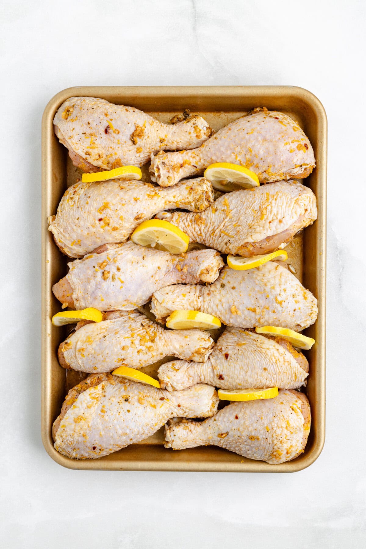 chicken drumsticks arranged on a baking sheet with lemon slices in between. 