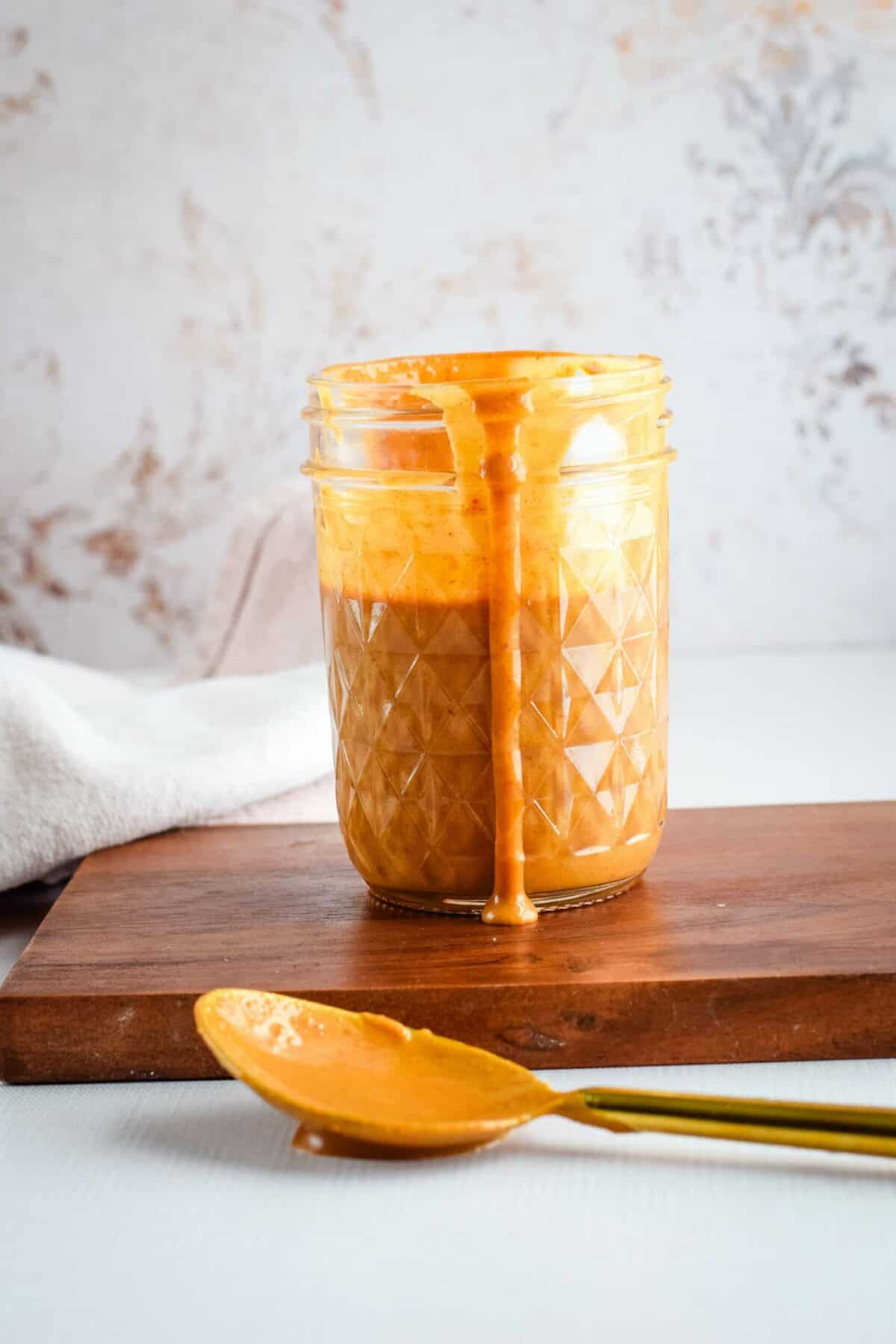 thai peanut sauce in a small mason jar with a spoon resting to the side.