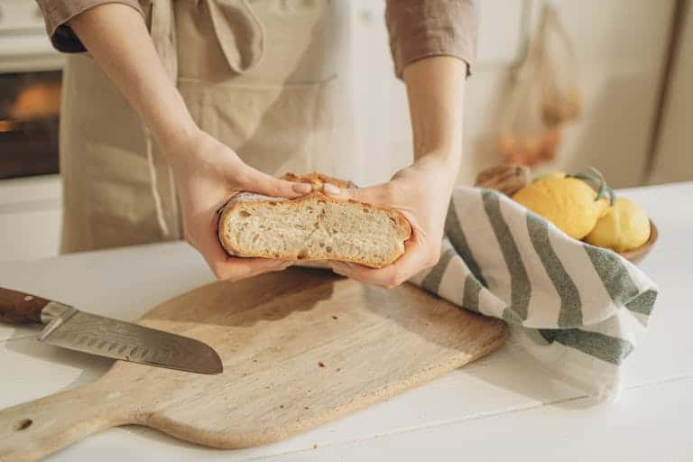 Close-up of hands holding sliced artisan bread on a wooden cutting board with lemons.