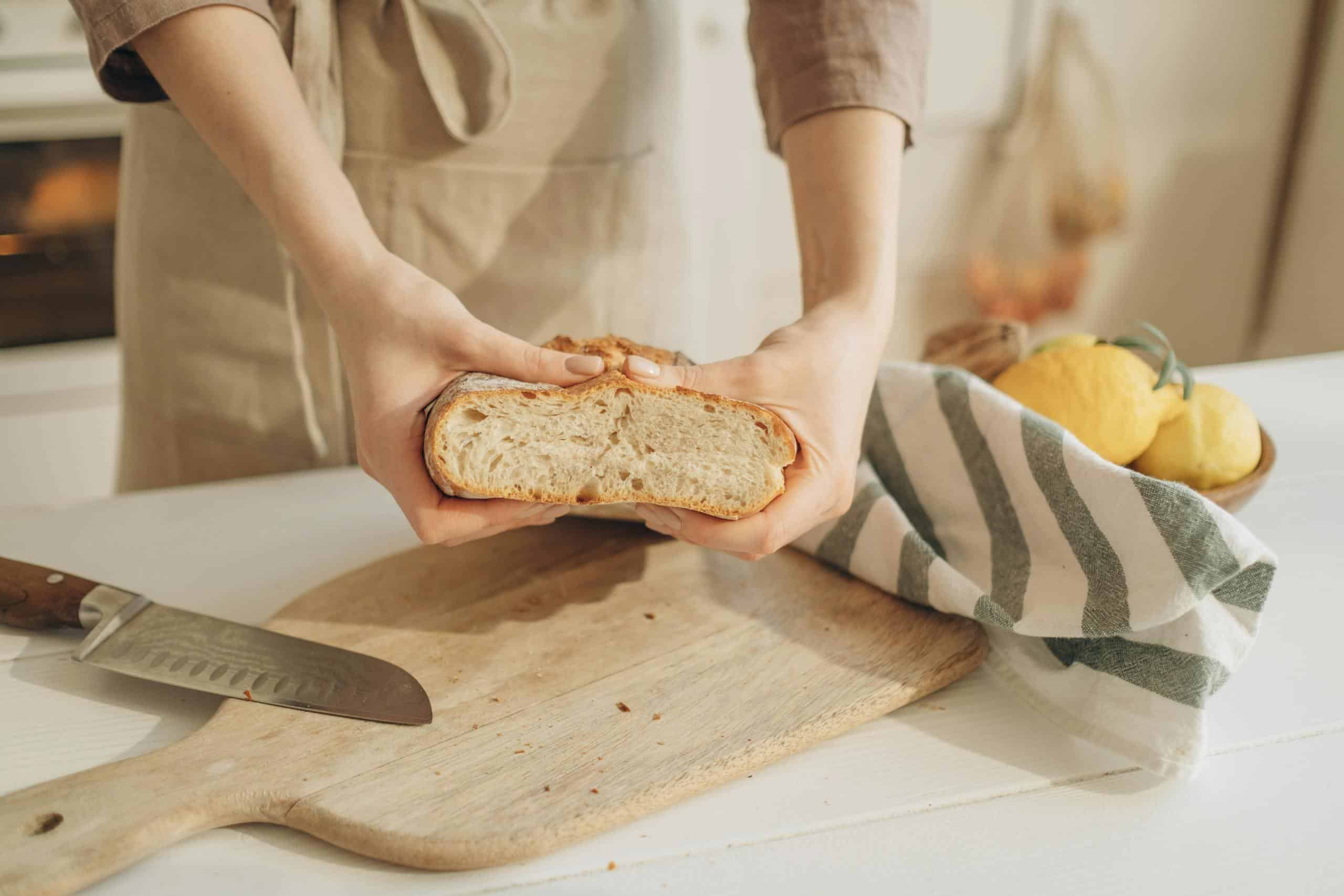 Close-up of hands holding sliced artisan bread on a wooden cutting board with lemons.