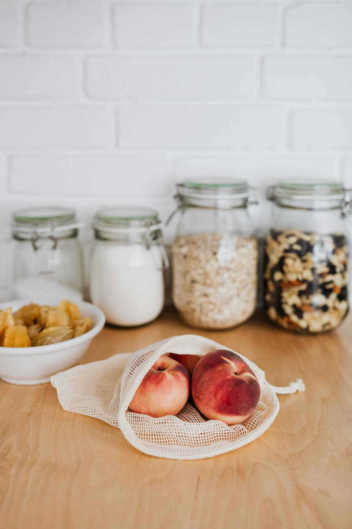 Eco-friendly kitchen storage featuring peaches in cotton bag and glass jars.