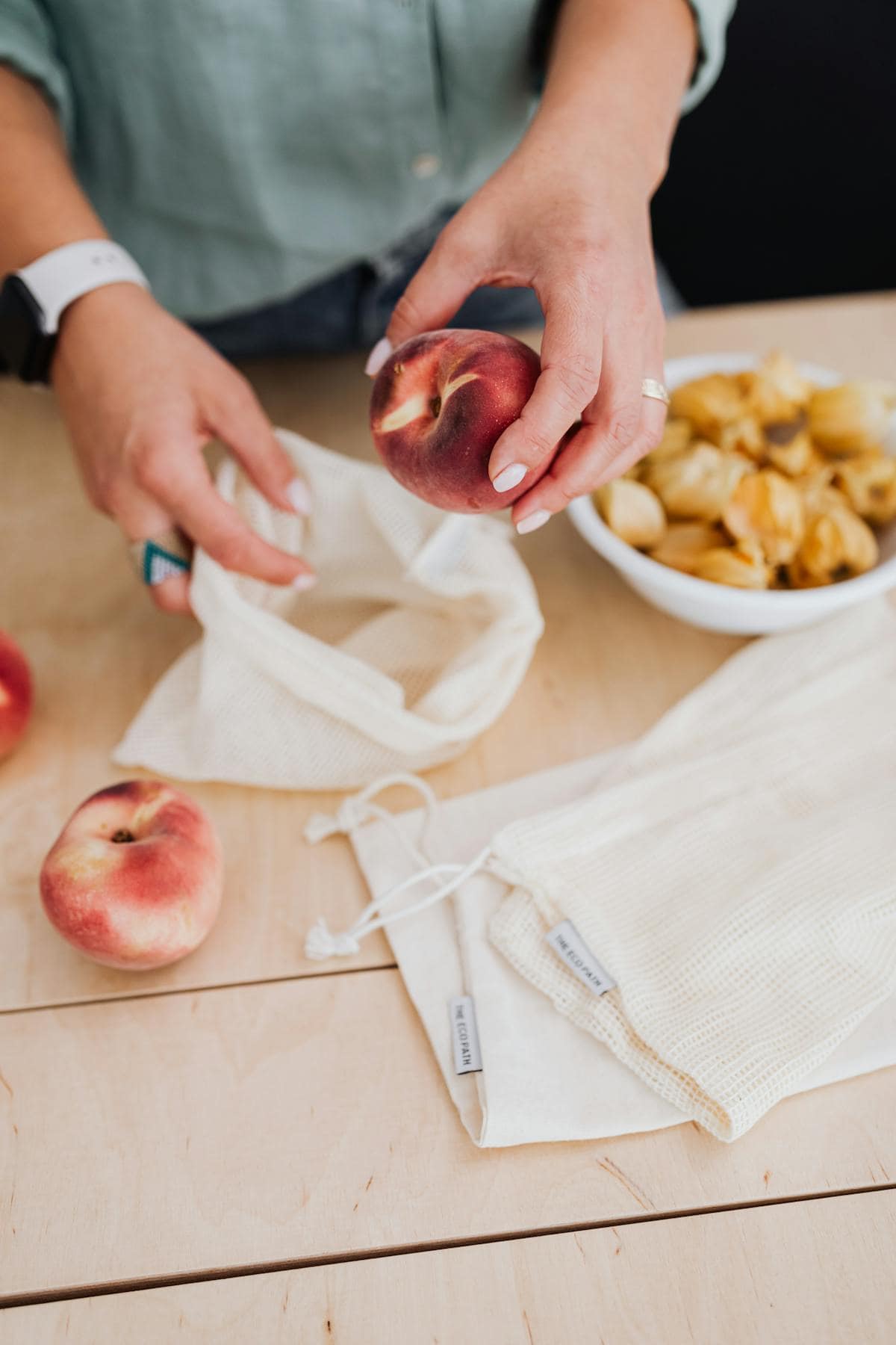 Person storing peaches in reusable cotton bags, promoting zero waste and eco-friendly living.