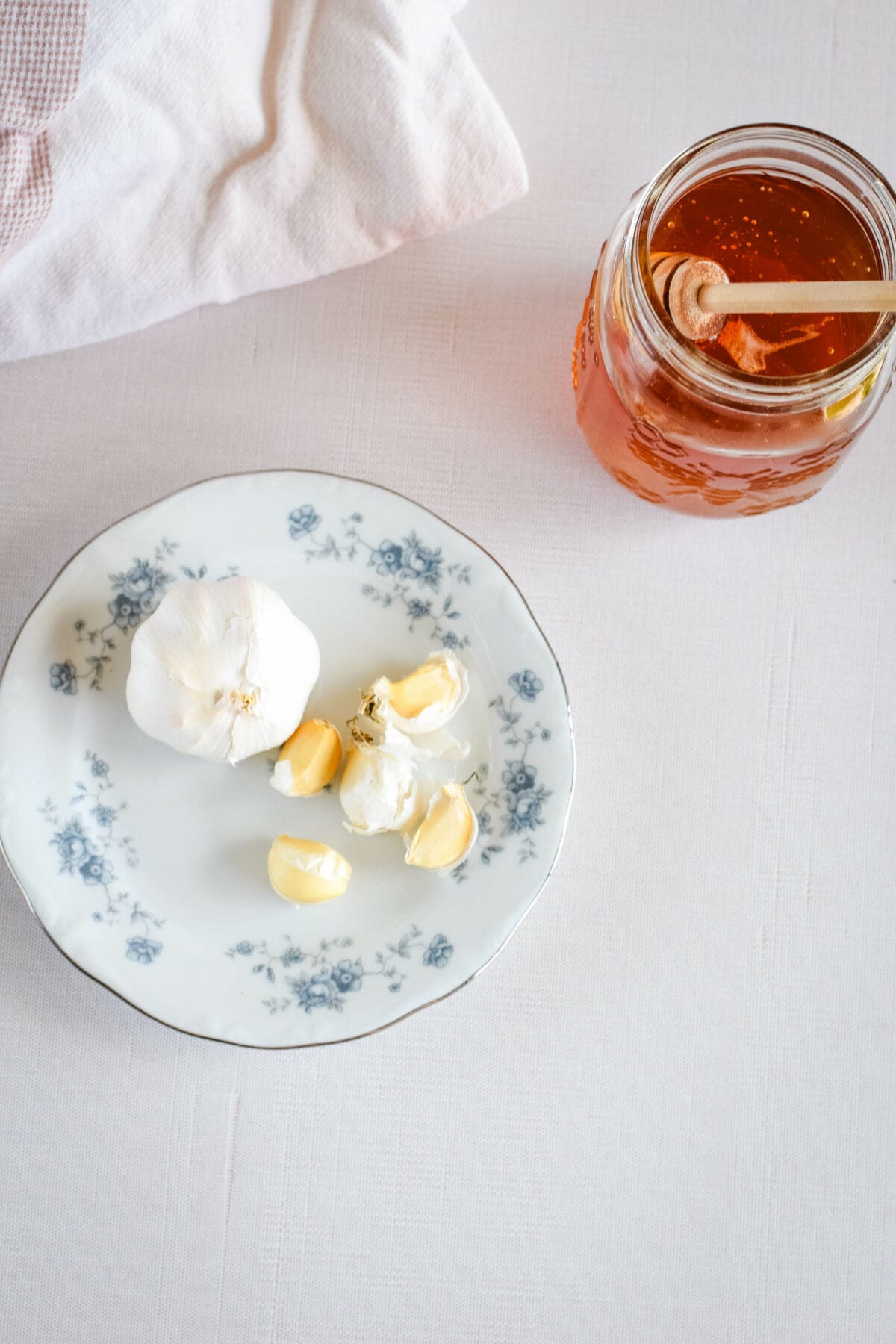 plate with garlic cloves and jar of honey on a table.