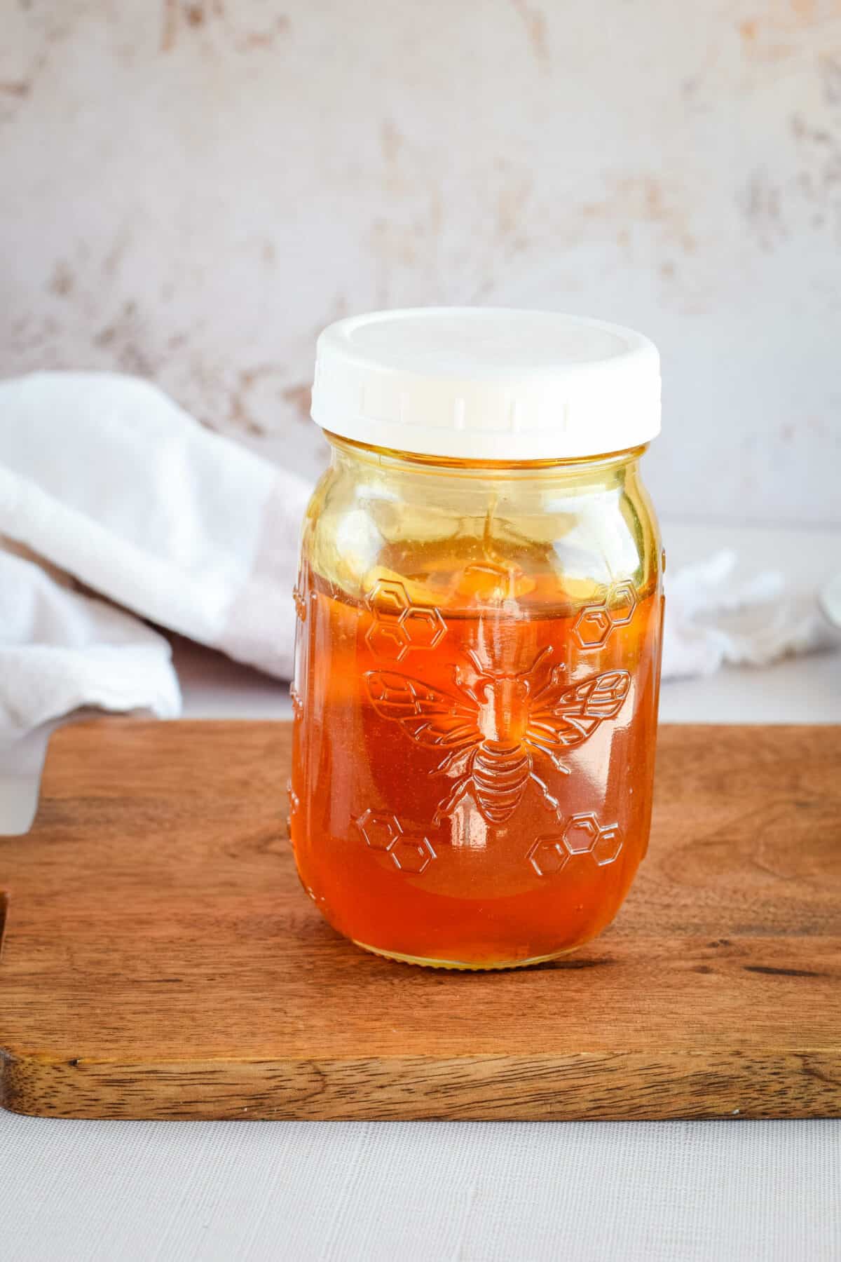 small mason jar filled with garlic infused honey on a wooden cutting board.